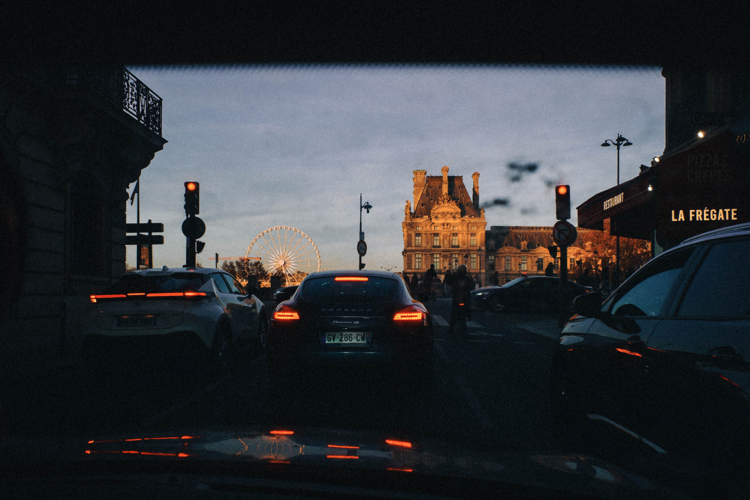 Cinematic sunset view of Paris traffic captured from the backseat of a taxi, with the Louvre glowing in golden light and the Ferris wheel rising in the distance. Shot by Wesley Verhoeve on a Fujifilm XF10.