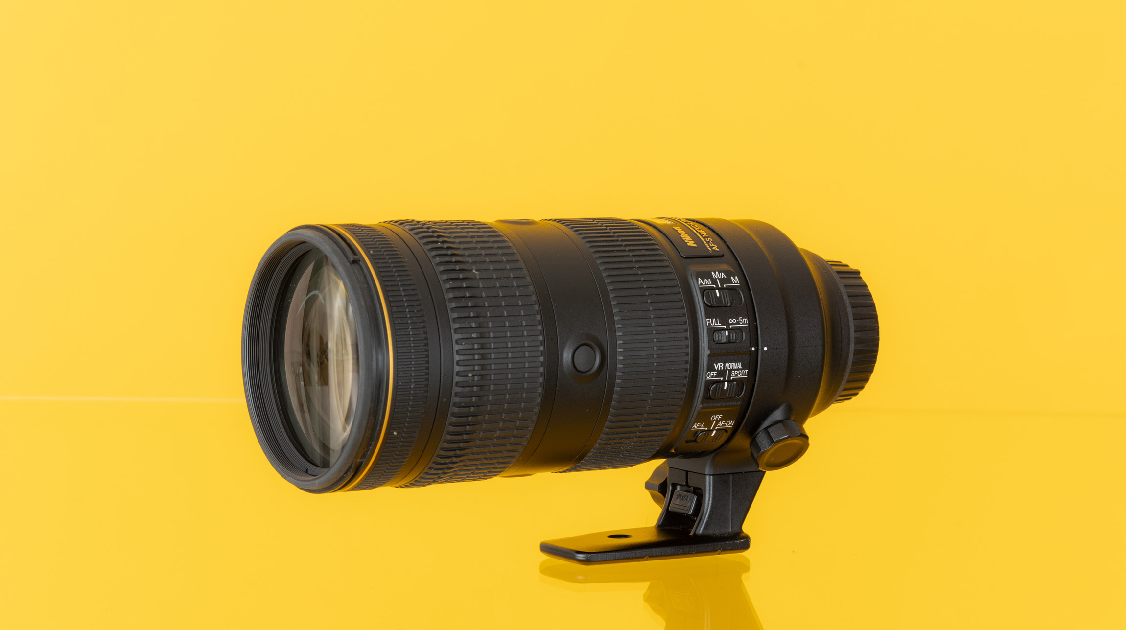 A photo of Nikon AF-S 70-200mm f/2.8E FL ED VR telephoto zoom lens against a yellow background