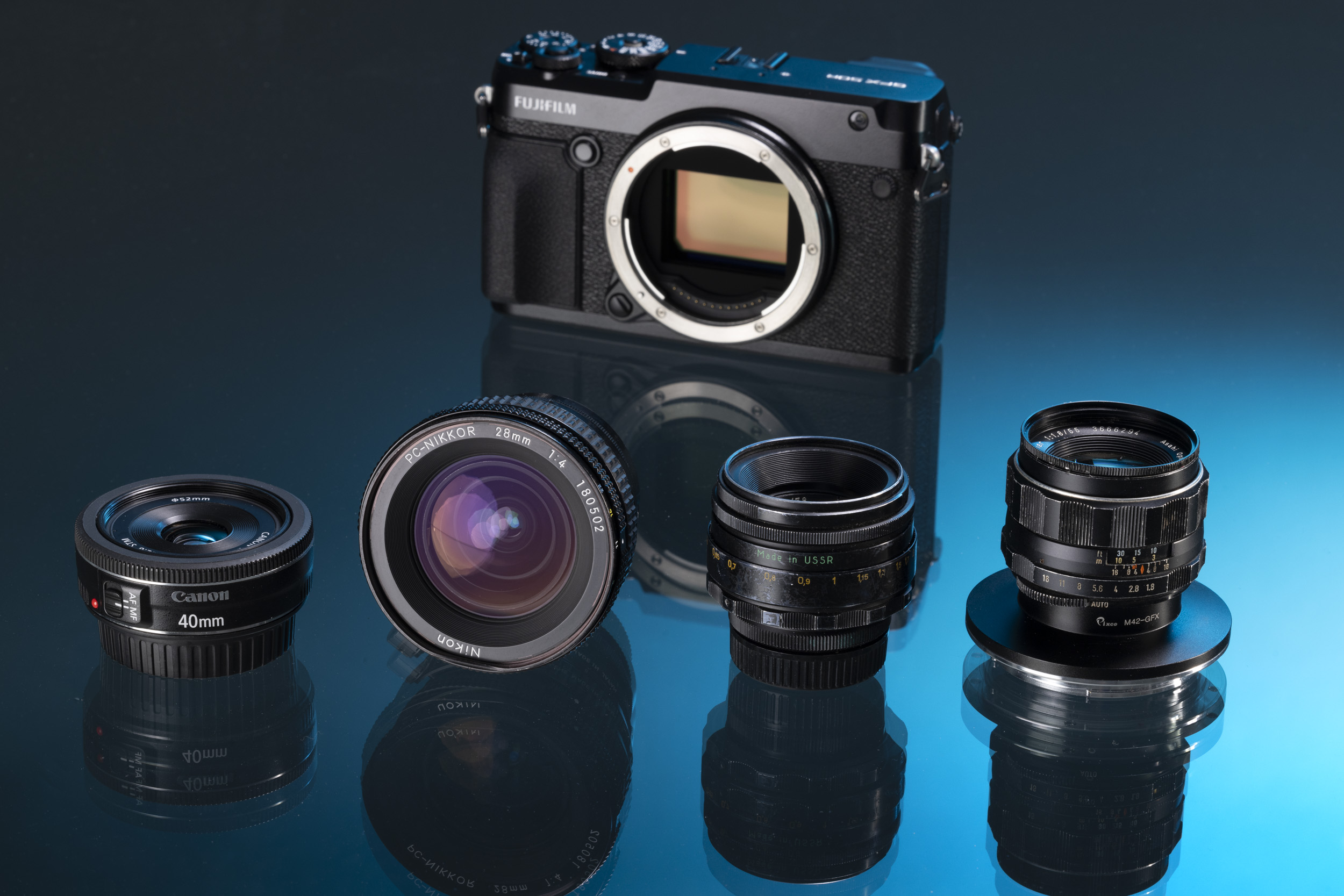 Une collection d’objectifs vintage est placée devant le Fujifilm GFX 50R — tu peux les adapter facilement à l’appareil.