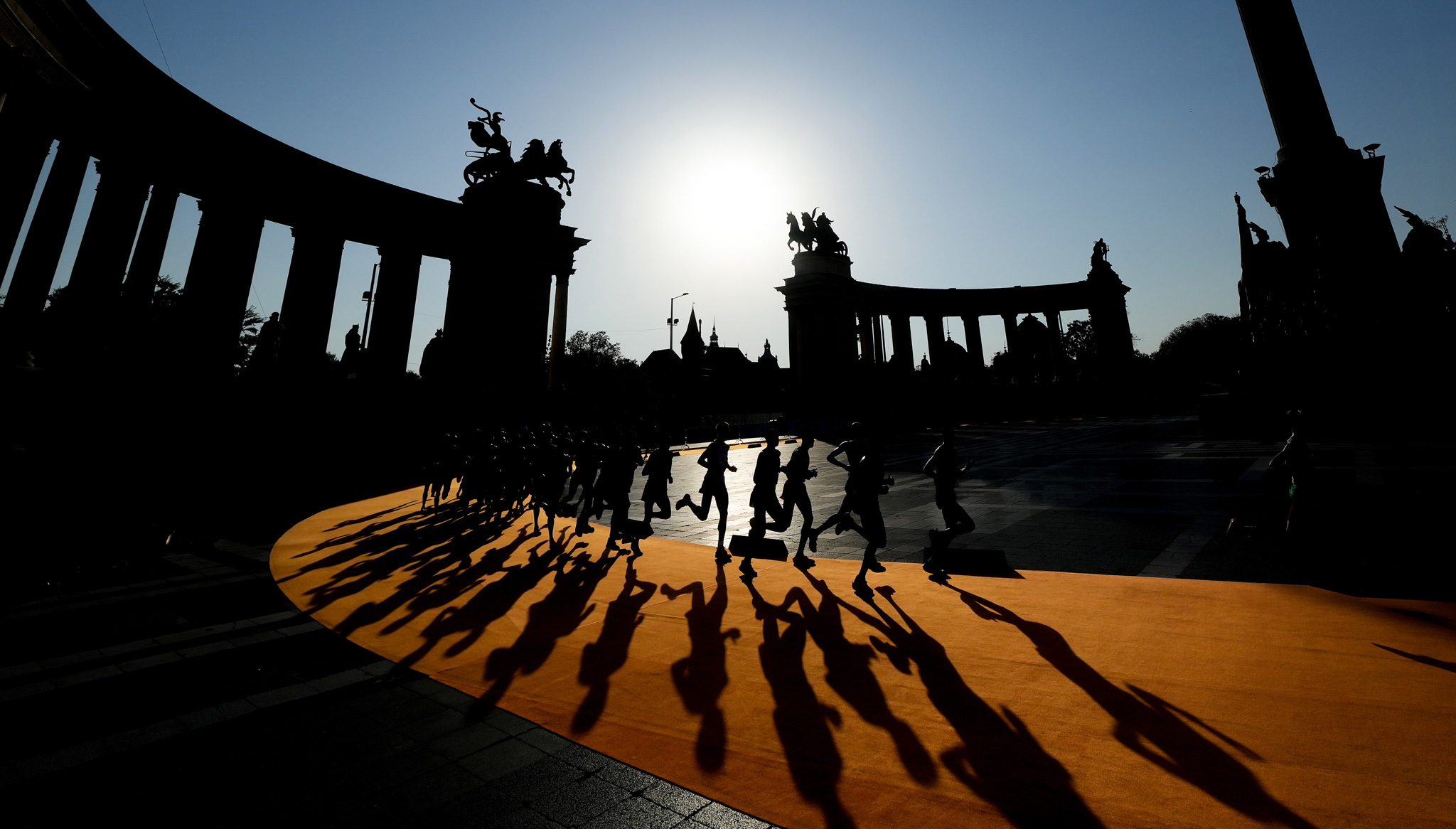 A group of runners casting long shadows on an orange track. By Martin Rickett. WSPA 2024 Shortlist.