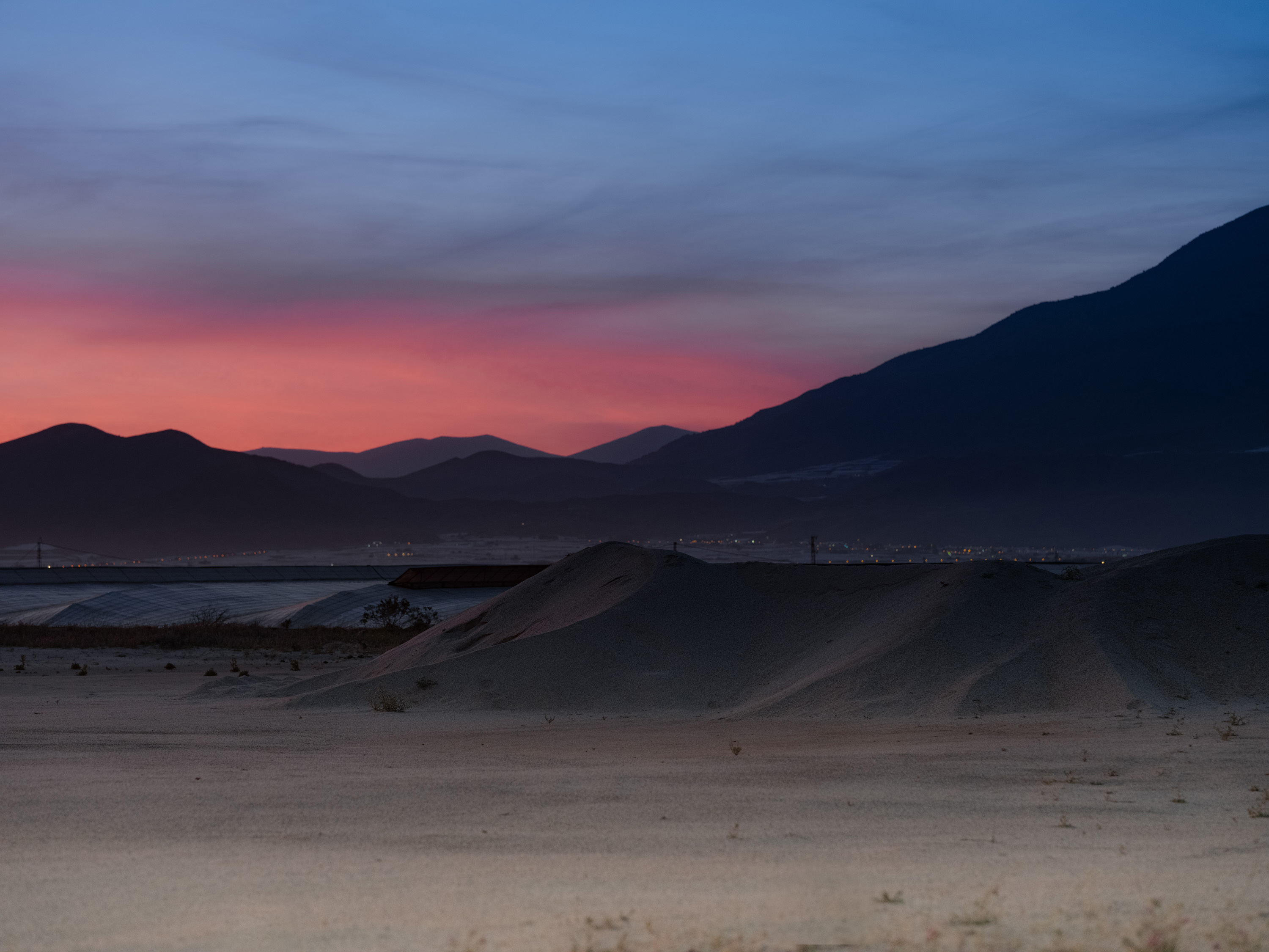 Pink and blue sunset over a desert, with a town in the distance.

