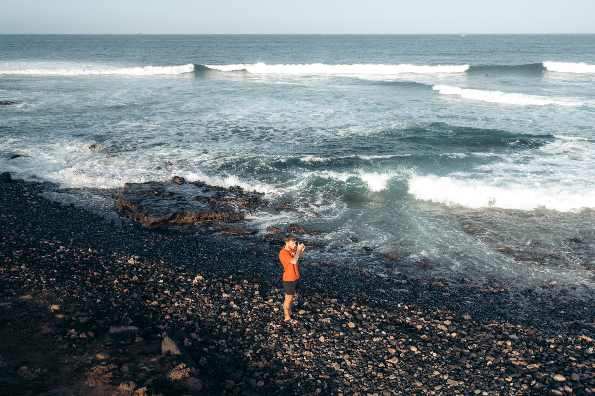 Travel photographer Harry Pope stands on a beach, surrounded by waves, holding the Canon EOS R5
