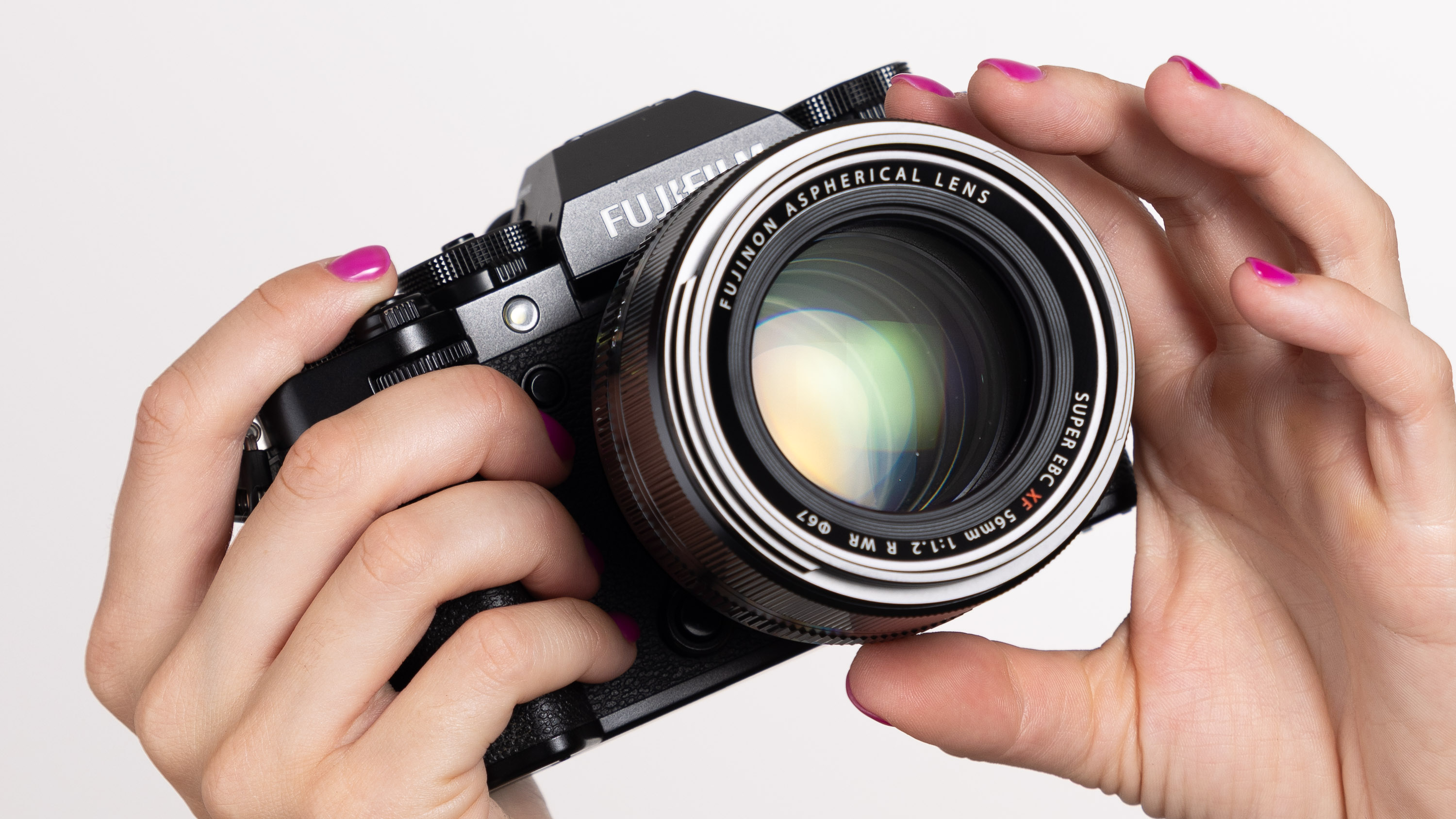 Hands holding up a second hand Fujifilm X-T5 and Fujifilm XF 56mm F/1.2 R WR on an off-white background