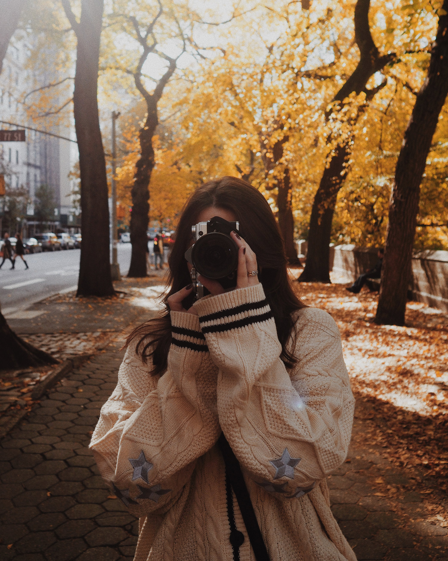 A photo of Georgina Lamrock taking a photo with the Olympus E-M5 III in Central Park with an avenue of trees and a road in the background