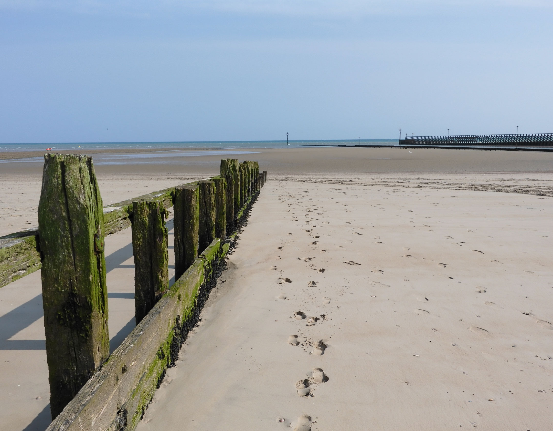 The beach at low tide, with footprints in the sand by the wooden groynes. 