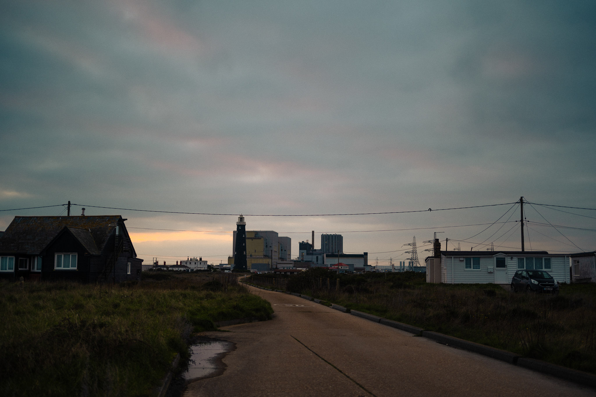 Moody coastal scene at dusk with a road leading towards a lighthouse and industrial buildings,, photographed with the Nikon Zf by Jakub Golis. 