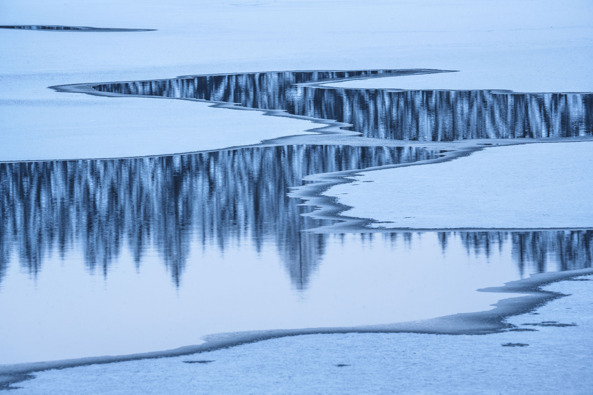 Small mountain lake in winter, in which fir trees are reflected, shot by Kilian Schönberger