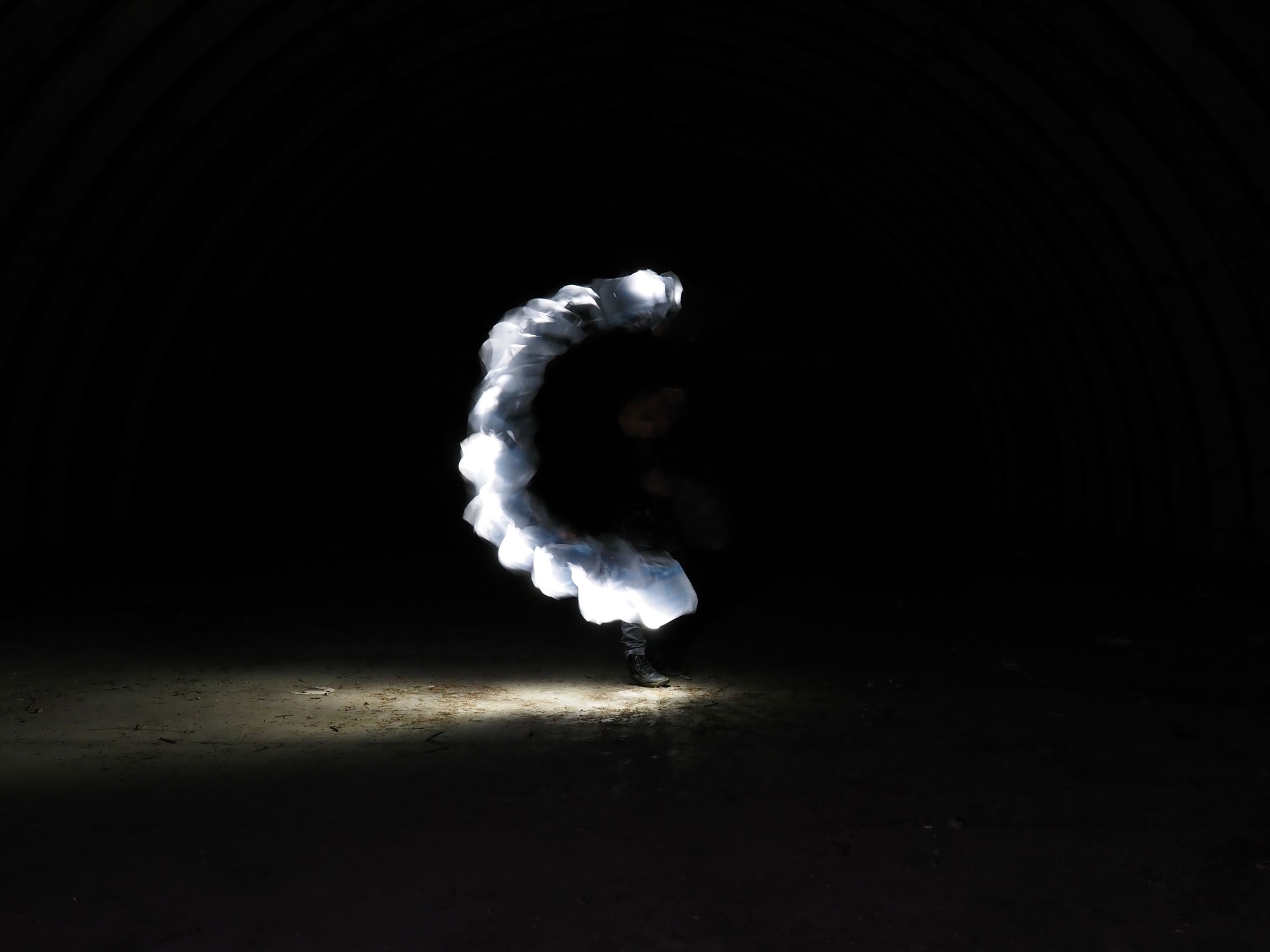 Lightpainting mit weißem Halbkreis vor dunklen Hintergrund, am unteren Ende des Halbkreises ist ein Fuß zu sehen, aufgenommen mit einer Olympus OM-D E-M5 Mark III im Bulb-Modus
