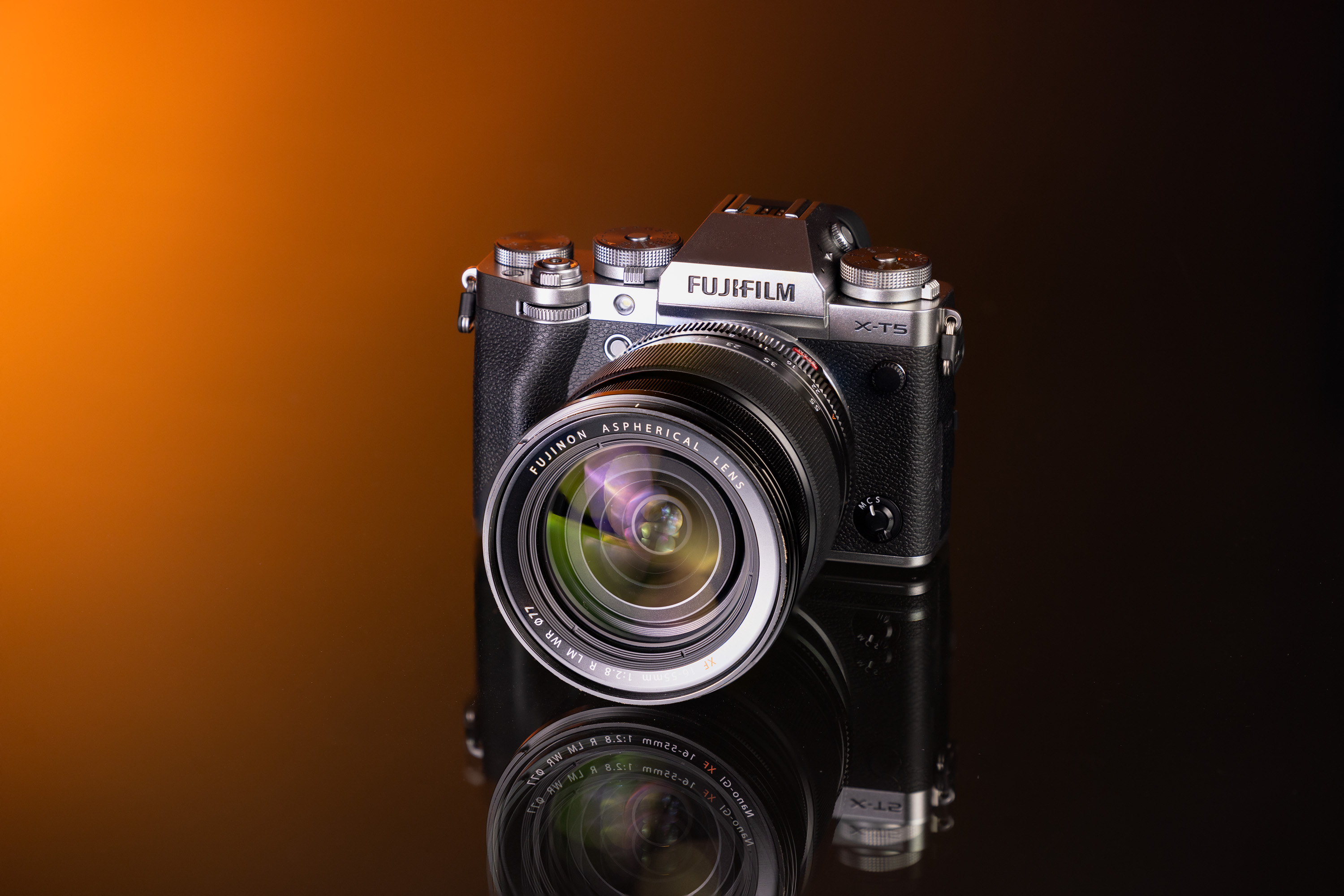 Gebrauchte Fujifilm X-T5 und Fujifilm XF 16-55mm f/2.8 R LM WR vor einem orange-schwarzen Hintergrund