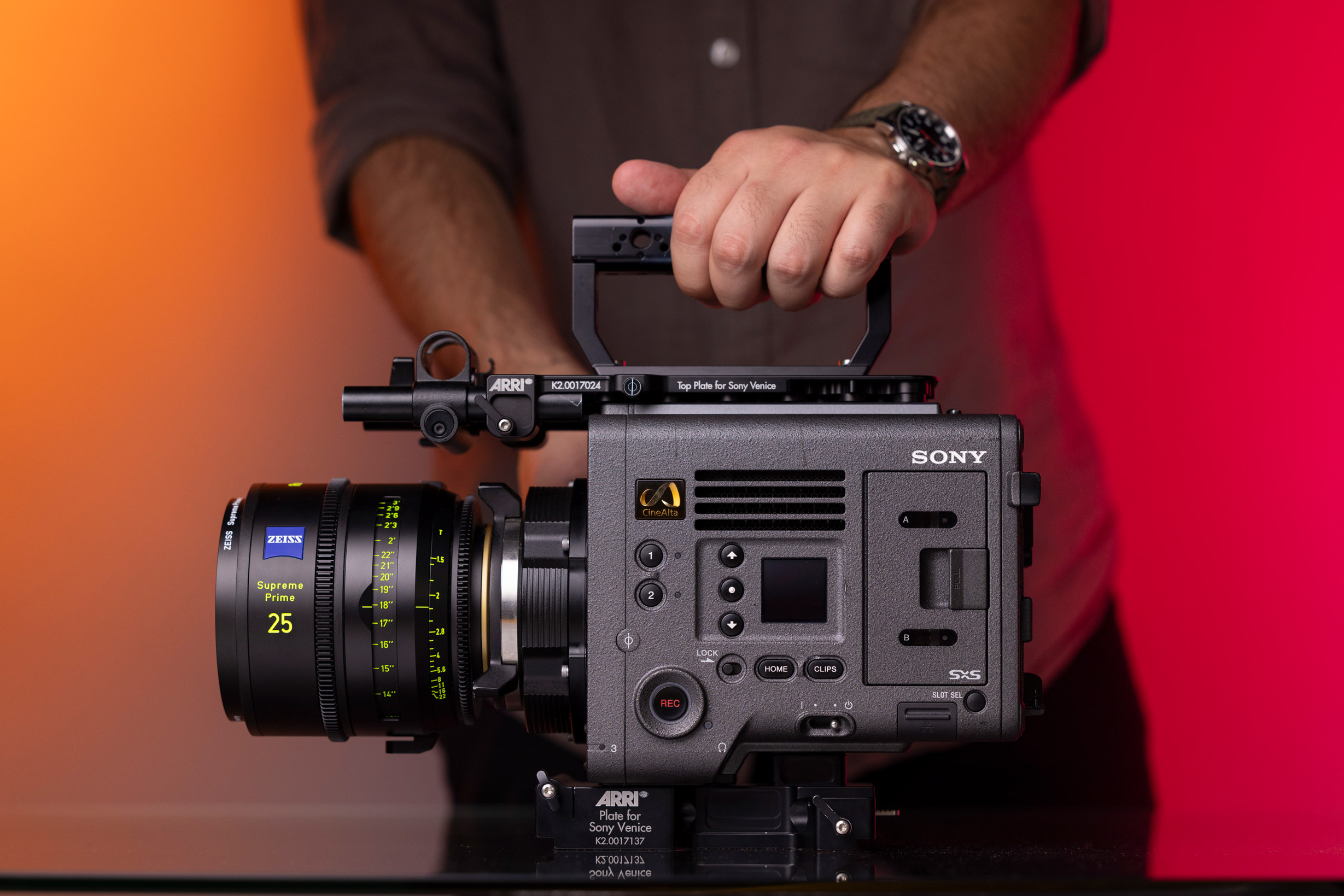 Hand with watch holding a Sony Venice camera on a red and orange background