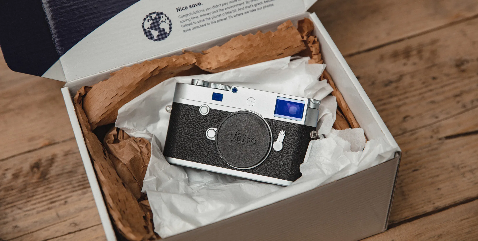 A black and grey Leica camera inside MPB plastic-free packaging on a wooden table
