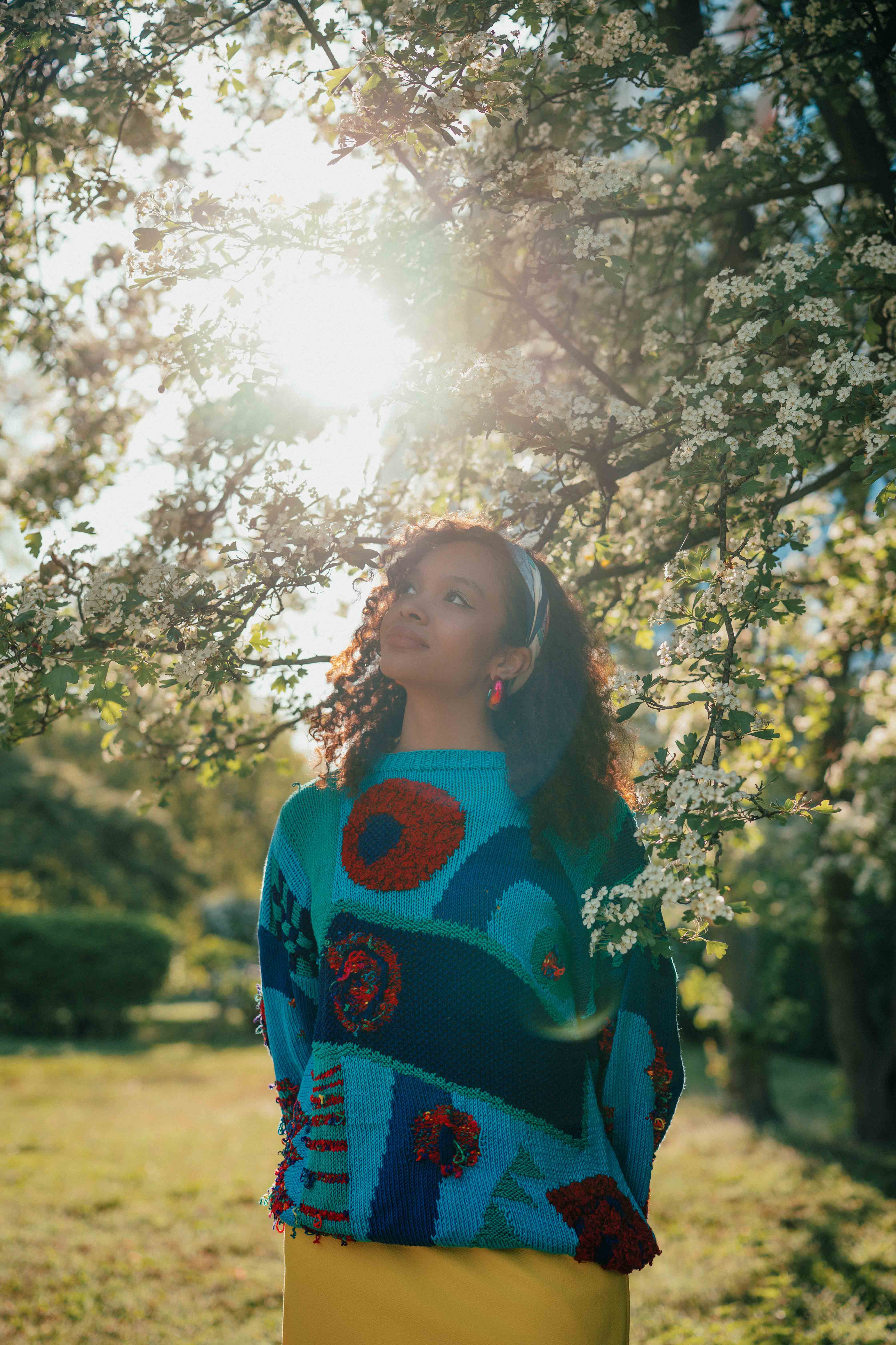 A model wearing a bold blue and red top, standing under a blossoming tree in Berlin’s Hansaviertel with the soft evening light behind her. Shot by Alina Rudya on a Nikon Z6 III.