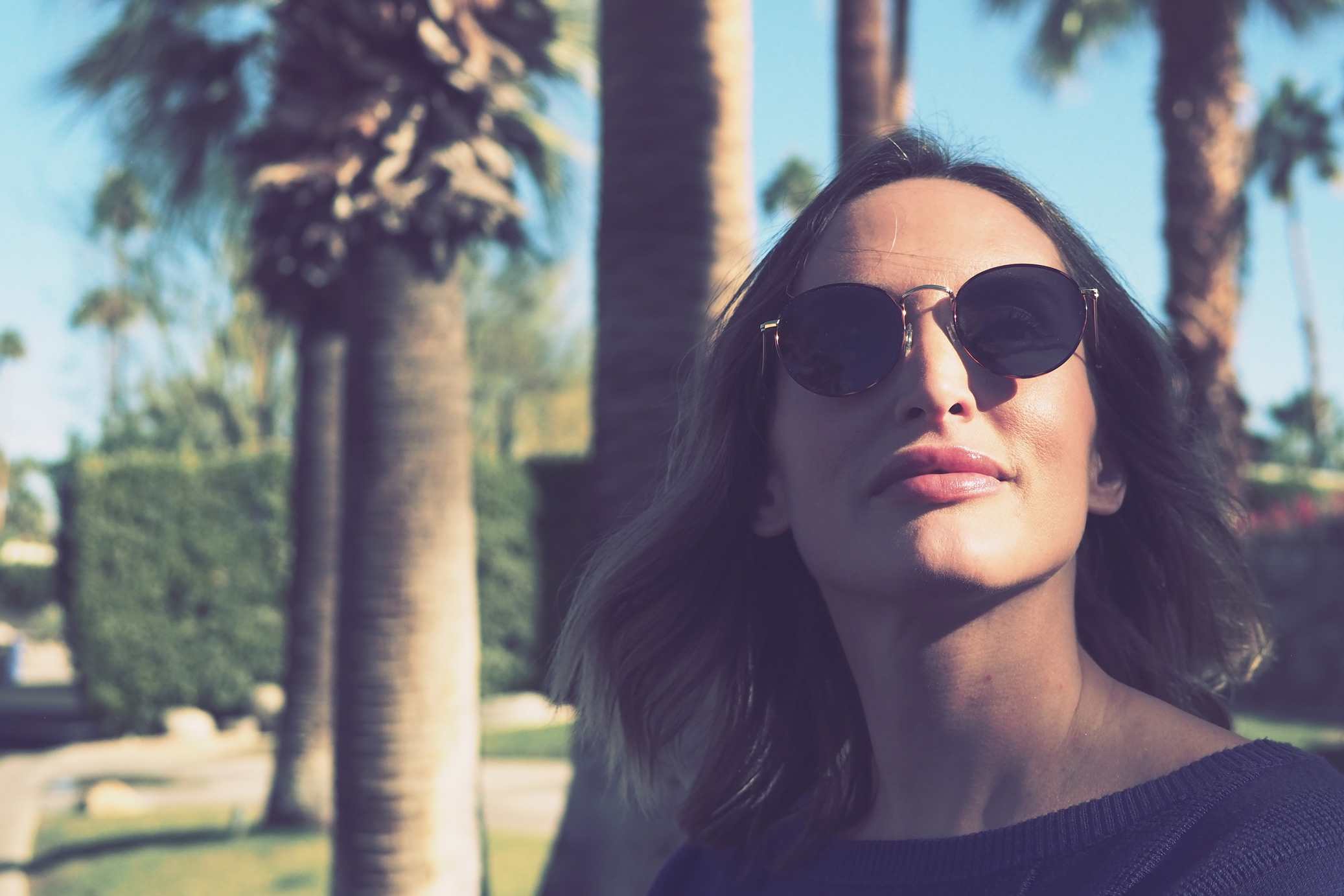 Woman standing with glasses and palm trees in the background in Palm Springs, California, taken on an Olympus Pen-F by Justin Patricolo.