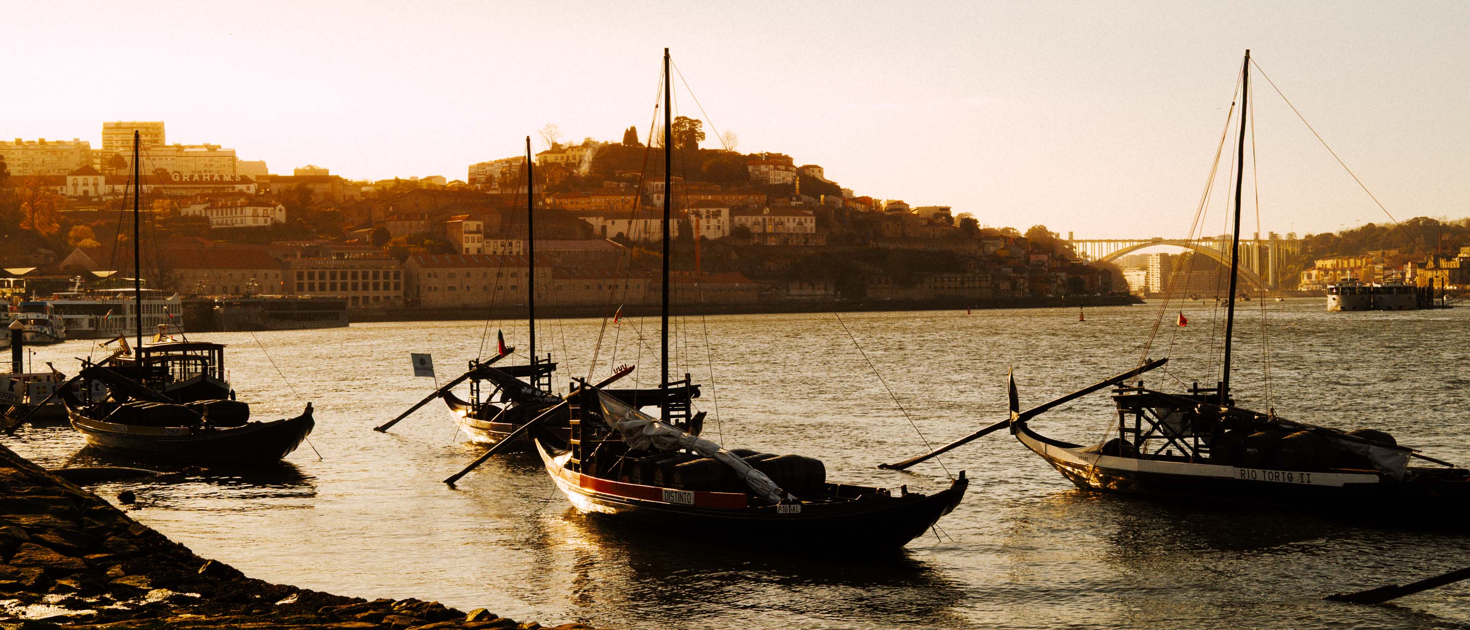 Breite Panoramaaufnahme der Uferpromenade von Porto im Format 21:9, mit traditionellen Rabelo-Booten im Vordergrund. Aufgenommen von Connor Redmond mit der Sigma BF.