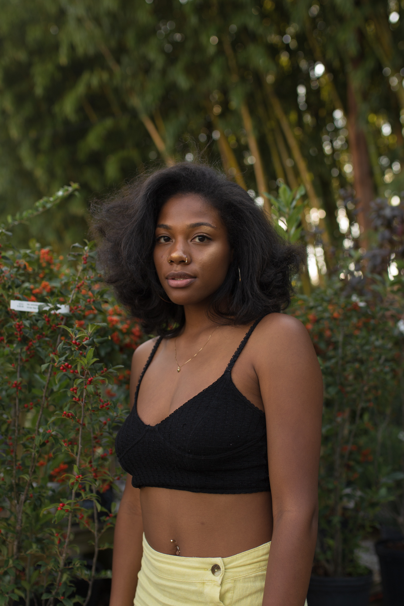 Photo of black woman outside with trees behind her wearing a black top and yellow shorts.