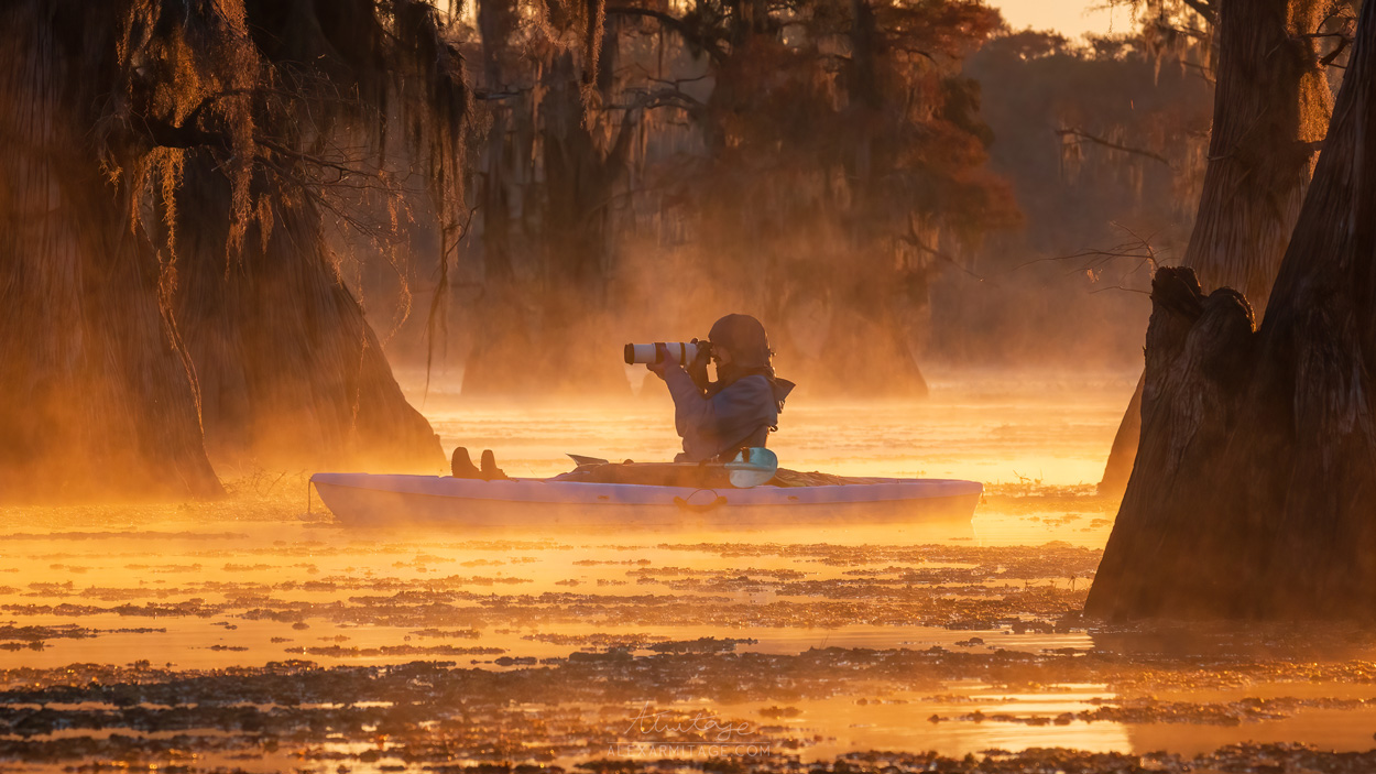 A person sits in a boat on a marshy body of water.