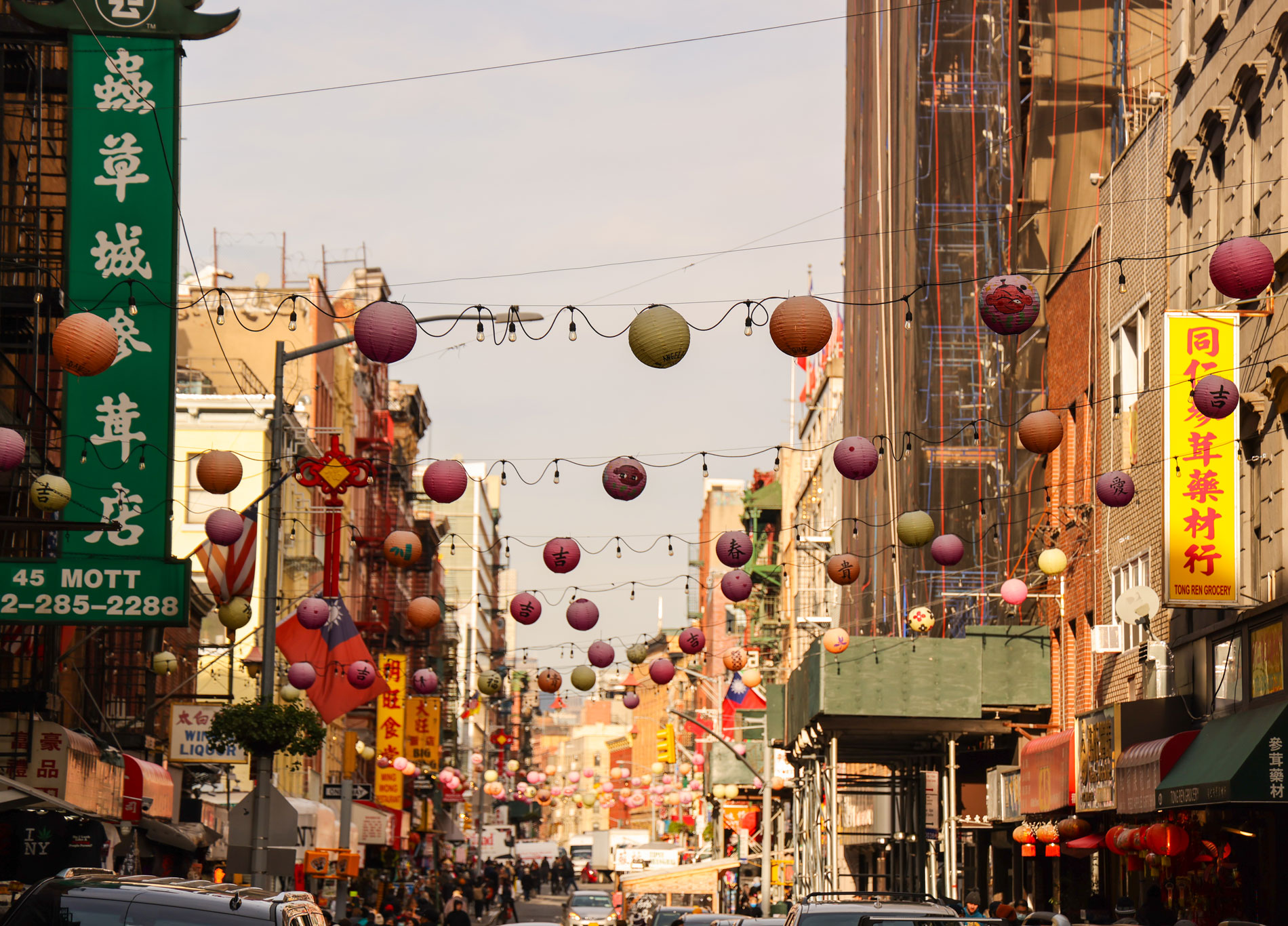 Street-level view of Chinatown in New York City with lights and lanterns hanging across the road, photo by Berta Amelinaite.