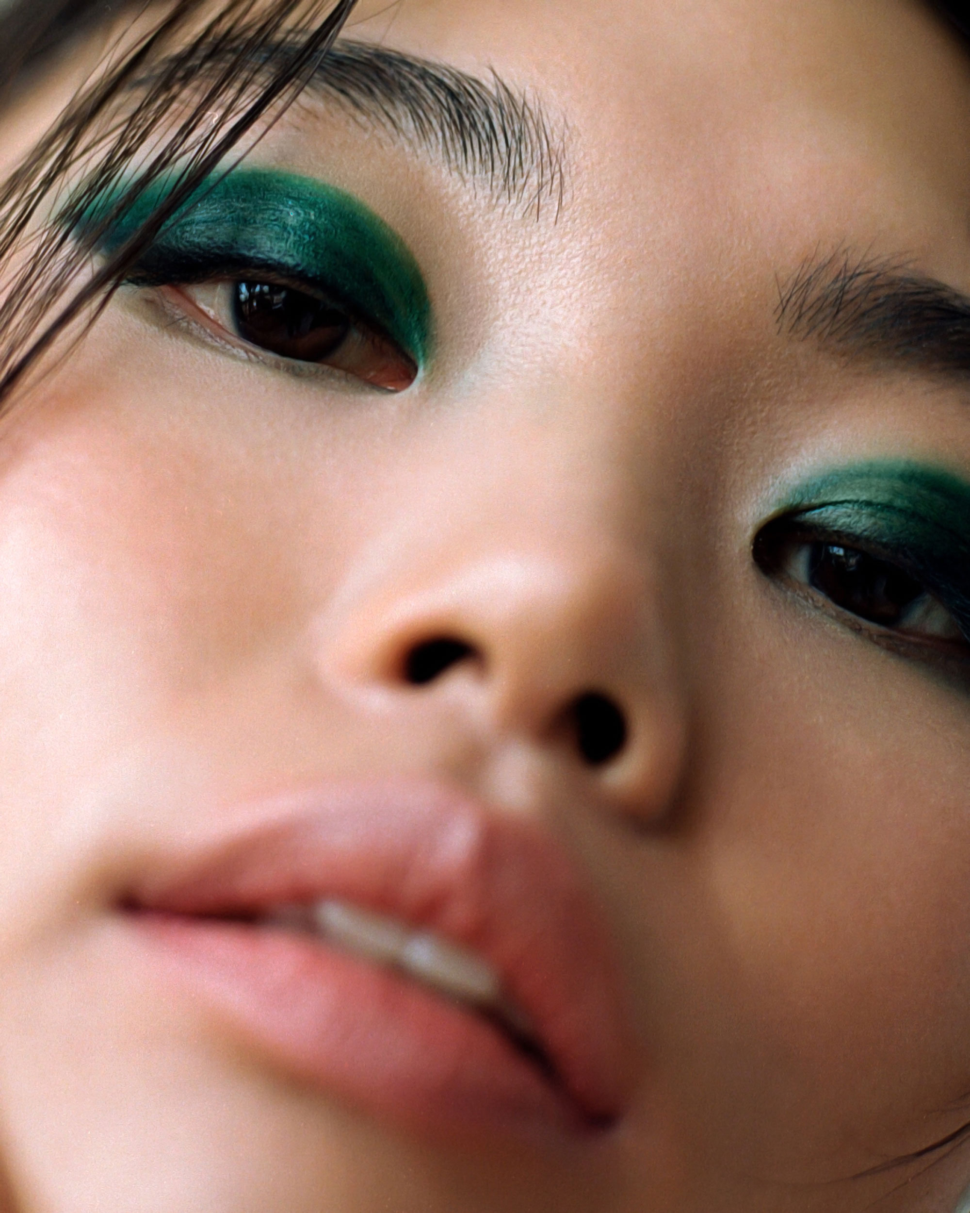 Gros plan du visage d'une femme avec du fard à paupières vert foncé sur toute la paupière et la bouche légèrement ouvert. Photo par Samia Rachel