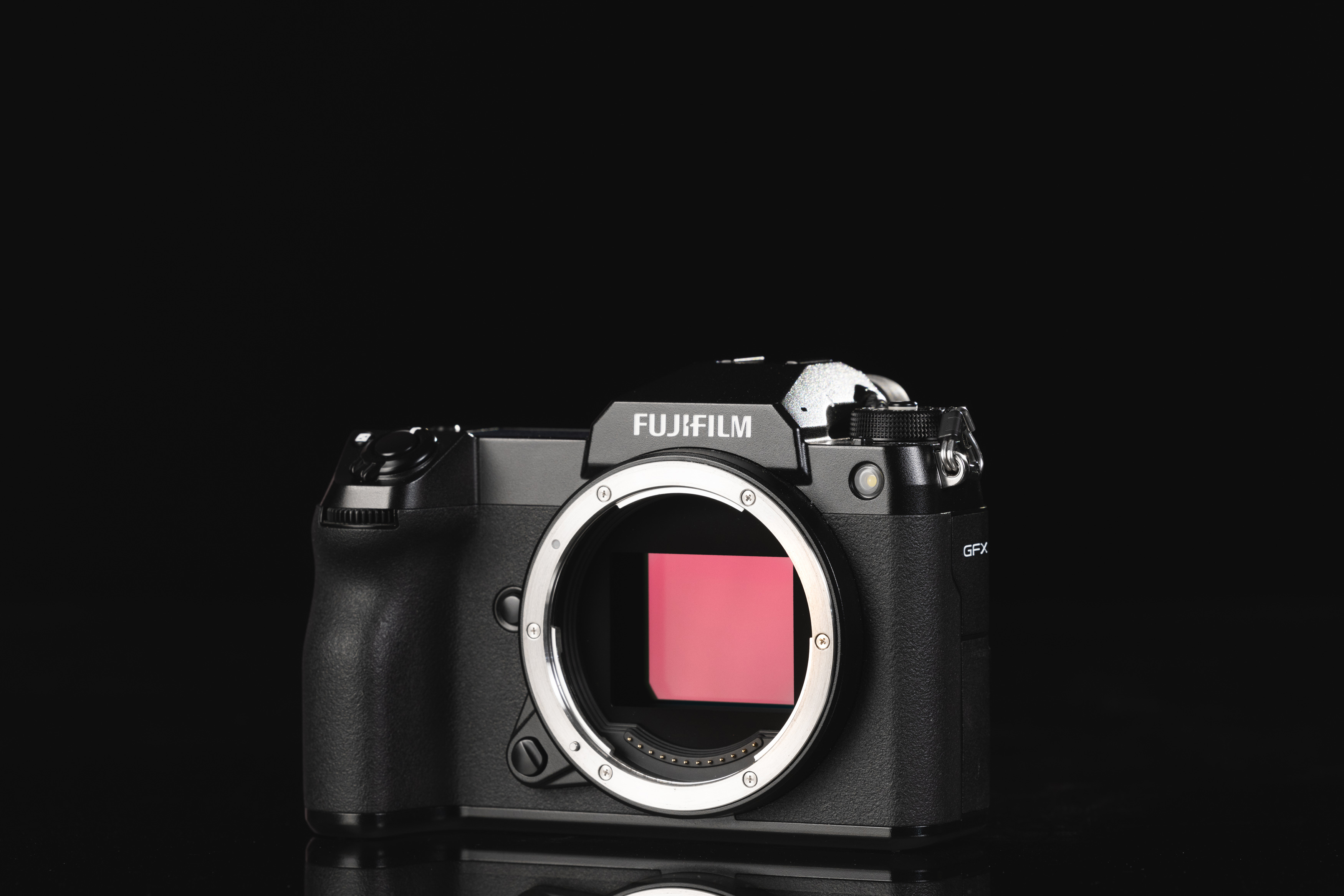 Frontansicht der Fujifilm GFX100S mit rosa Sensorreflexion auf schwarzem Hintergrund