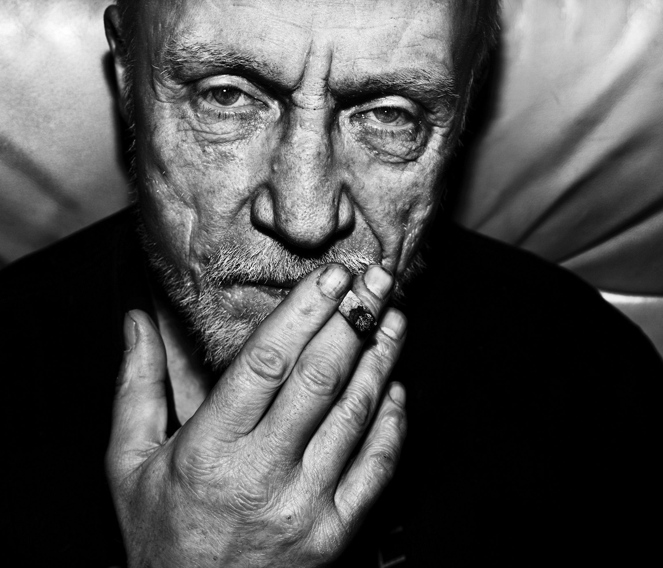 Black and white shot of a person smoking and looking directly into the camera with a serious expression on their face, photo by Jens Juul

