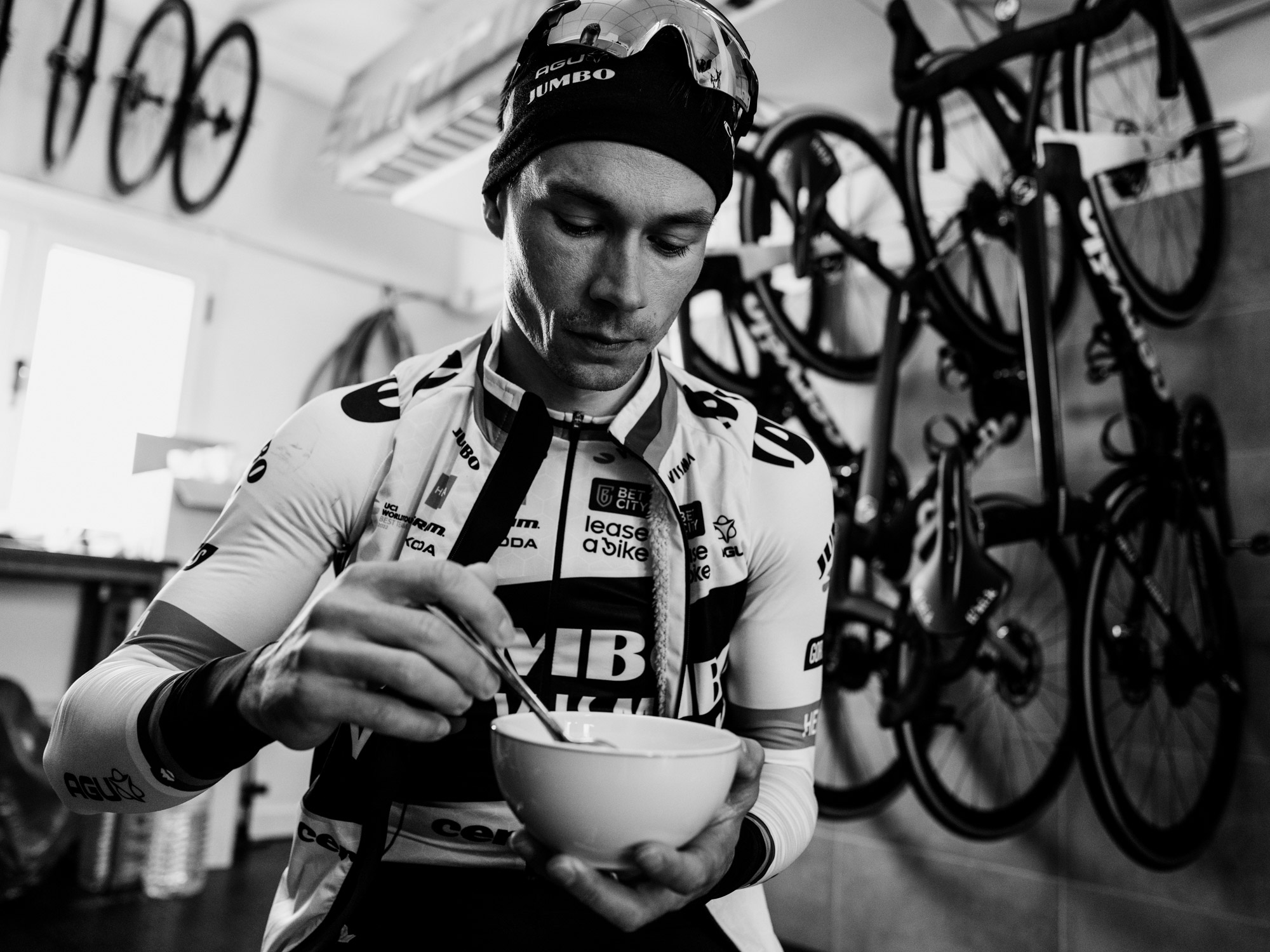 Un coureur de l’équipe Jumbo Visma prend son repas entouré de vélos, dans une scène documentaire en noir et blanc capturant un moment du quotidien loin de la compétition. Photo : Dan King, réalisée avec un Fujifilm X-Pro 3.