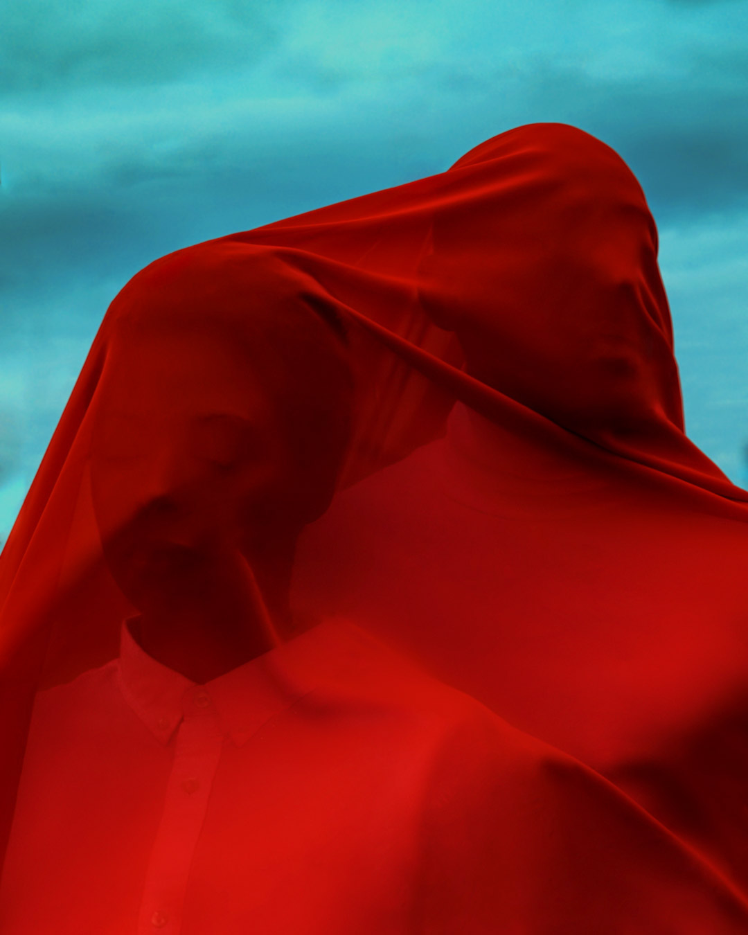 Two models completely covered in red fabric posing in front of a light-blue background, shot by Monica Krystel Rose with a Sony A7R III