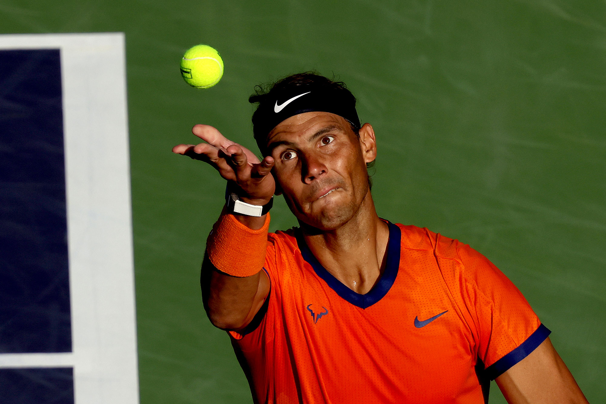 Rafael Nadal of Spain serves to Nick Kyrgios of Australia during the quarterfinals of the BNP Paribas Open at the Indian Wells Tennis Garden in Indian Wells, California. Only the ball is in the frame after being thrown in the air, with Nadal’s face focused.
