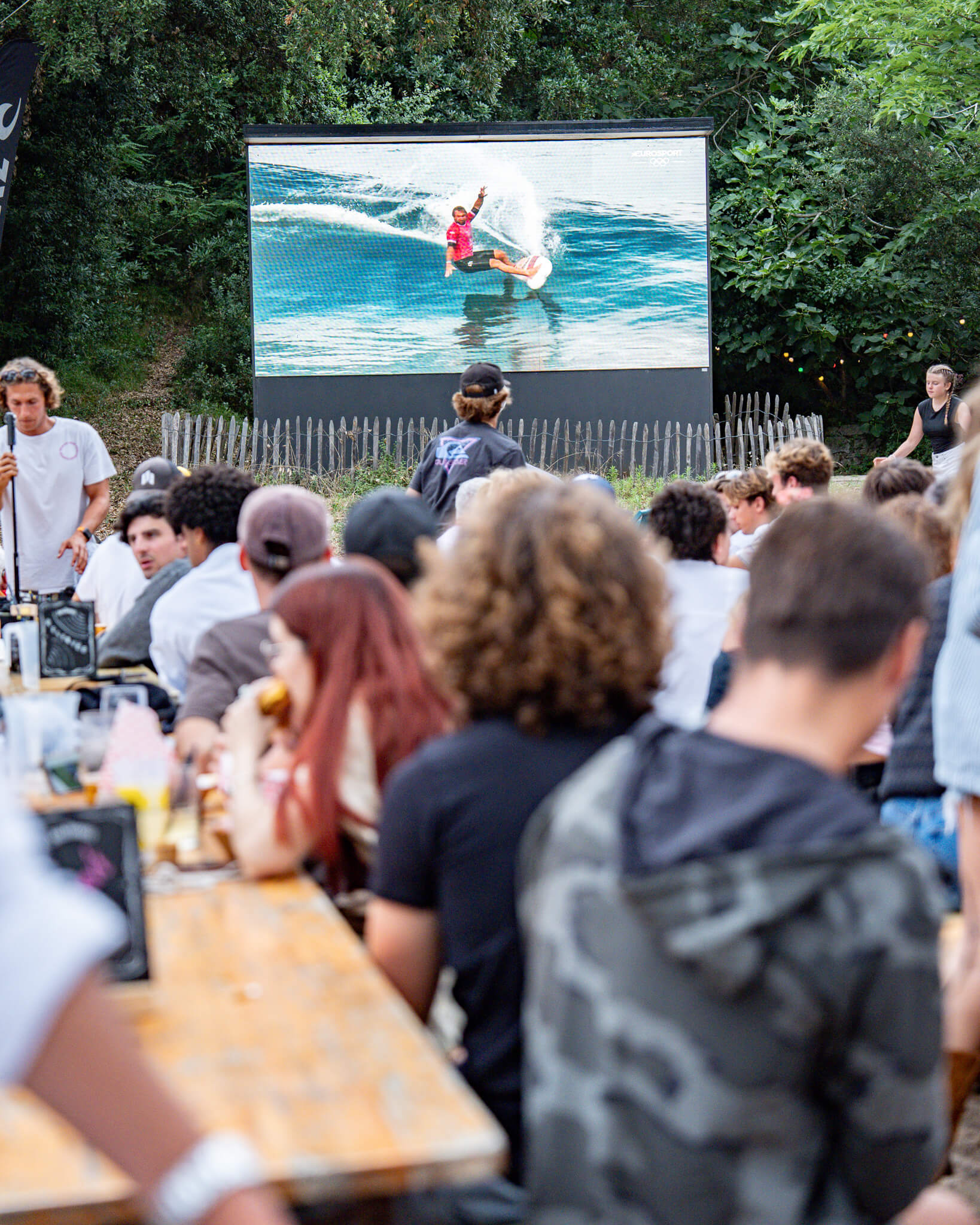
Des festivaliers sont assis sur des transats devant un écran sur lequel on peut voir un surfeur en action pendant le festival. Photo prise avec Sony A9 III par Paul Lavoine.

