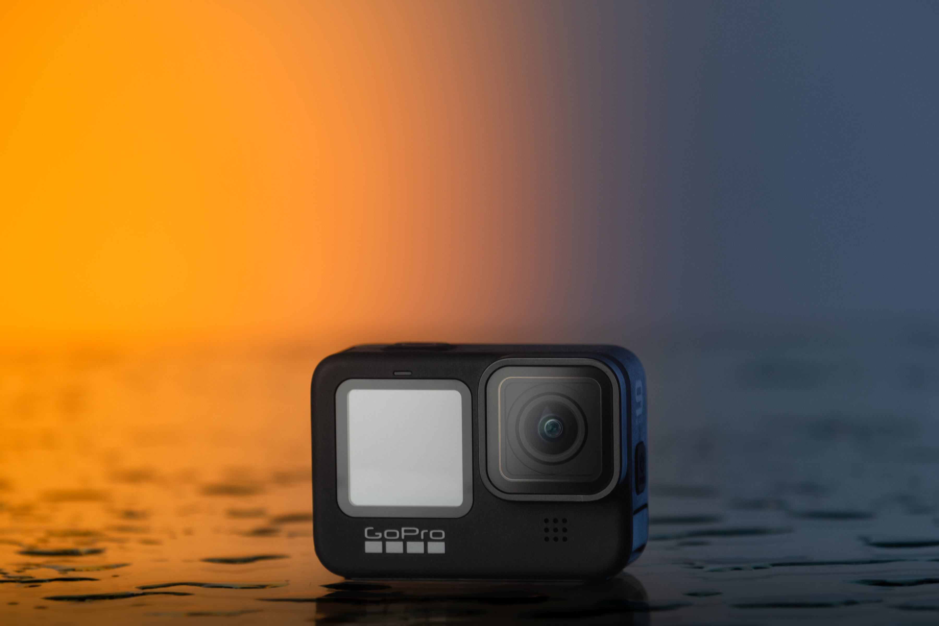 Bild einer GoPro Hero 9 mit orangefarbenem Sonnenuntergangs-Hintergrund auf einem nassen Tisch. 