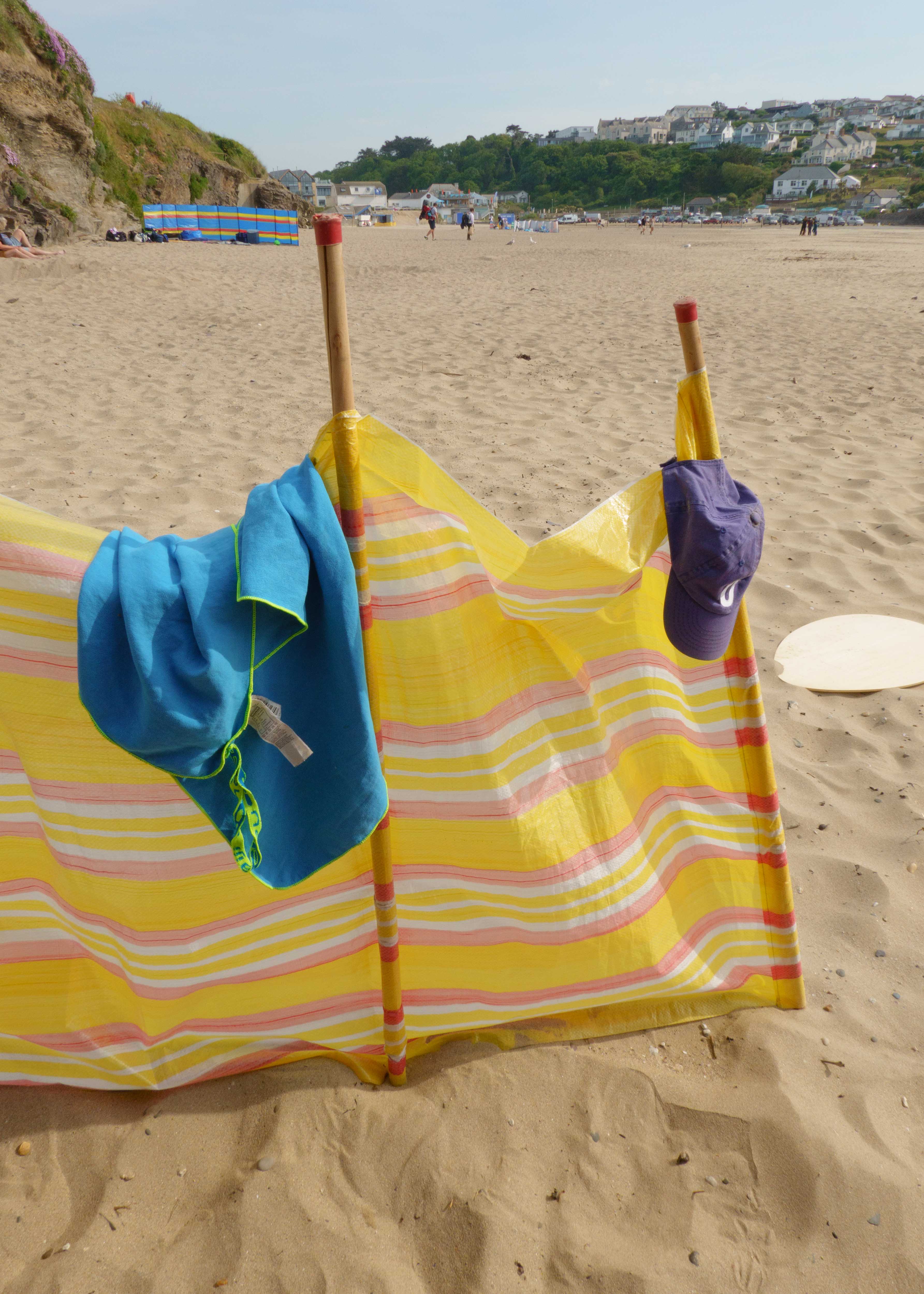Windscherm met hoed en handdoek erover gedrapeerd op het strand