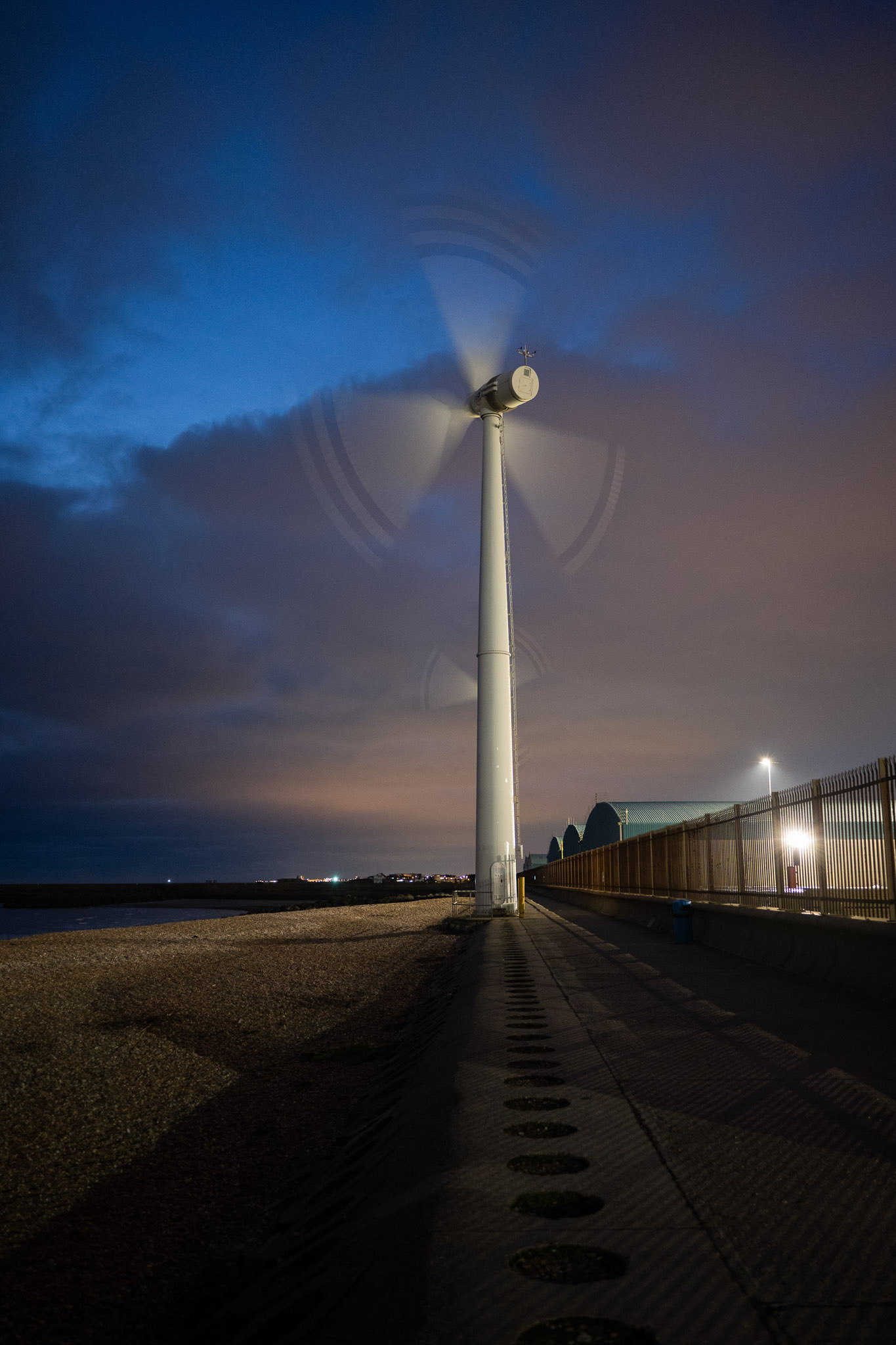 Wind turbine spinning at dusk beside a pebble beach, photographed with the Nikon Zf by Amy Moore. 
