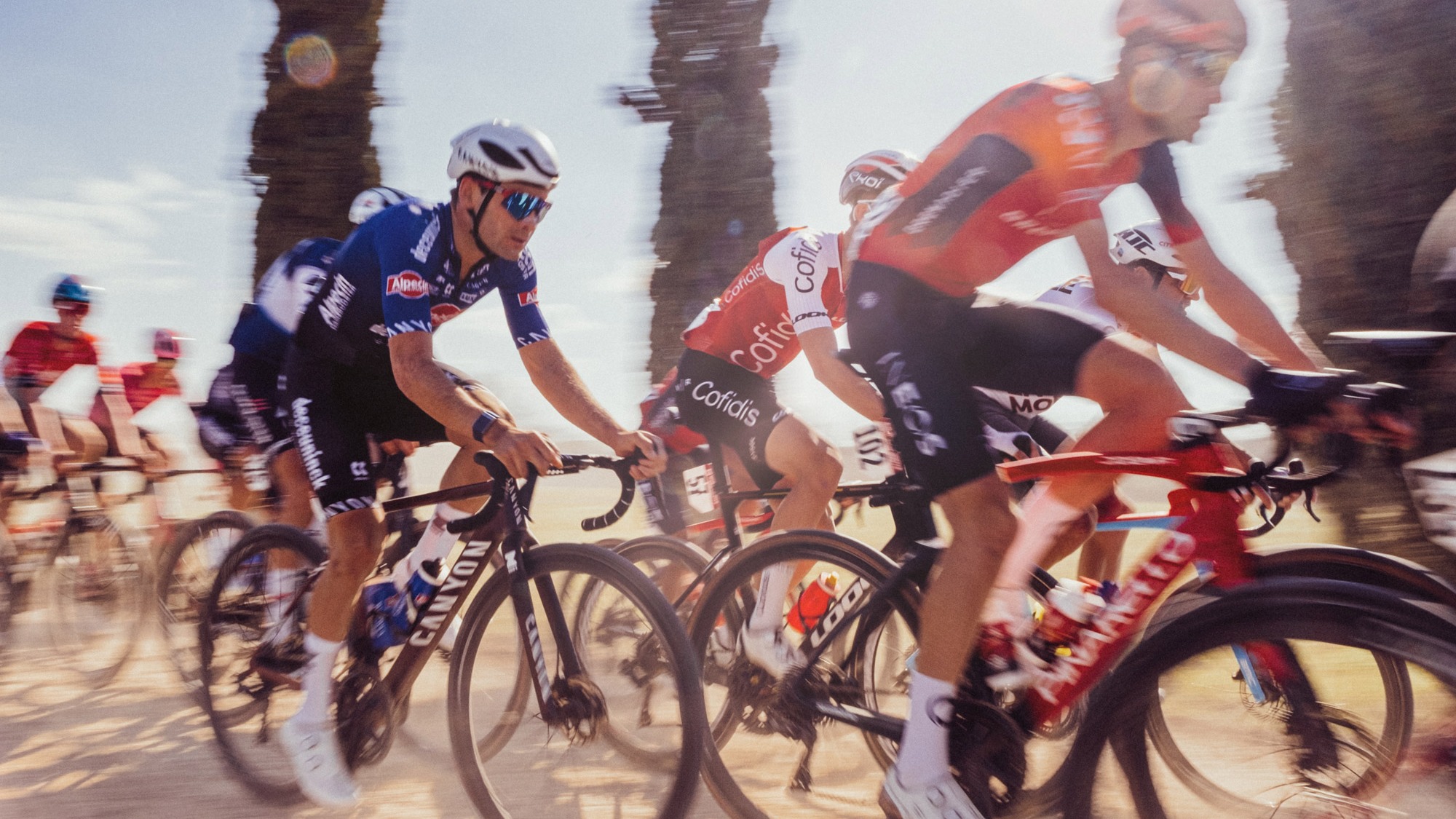 A motion-blurred photo of a group of cyclists from Team Jumbo Visma cycling along a dirt road, shot by Dan King with a Fujifilm X-Pro 3

