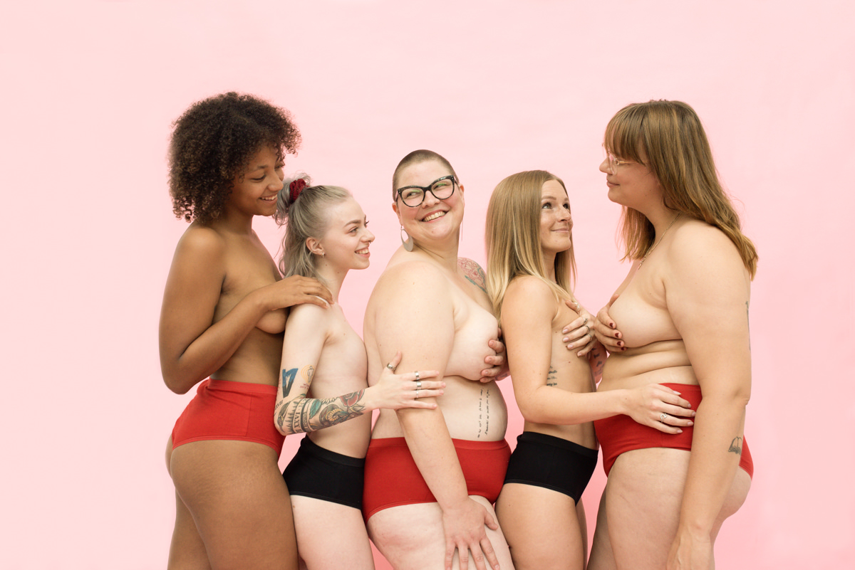 Une image où l’on voit cinq femmes serrées les unes contre les autres, vêtues de sous-vêtements noirs et rouges, se tenant devant un fond rose.