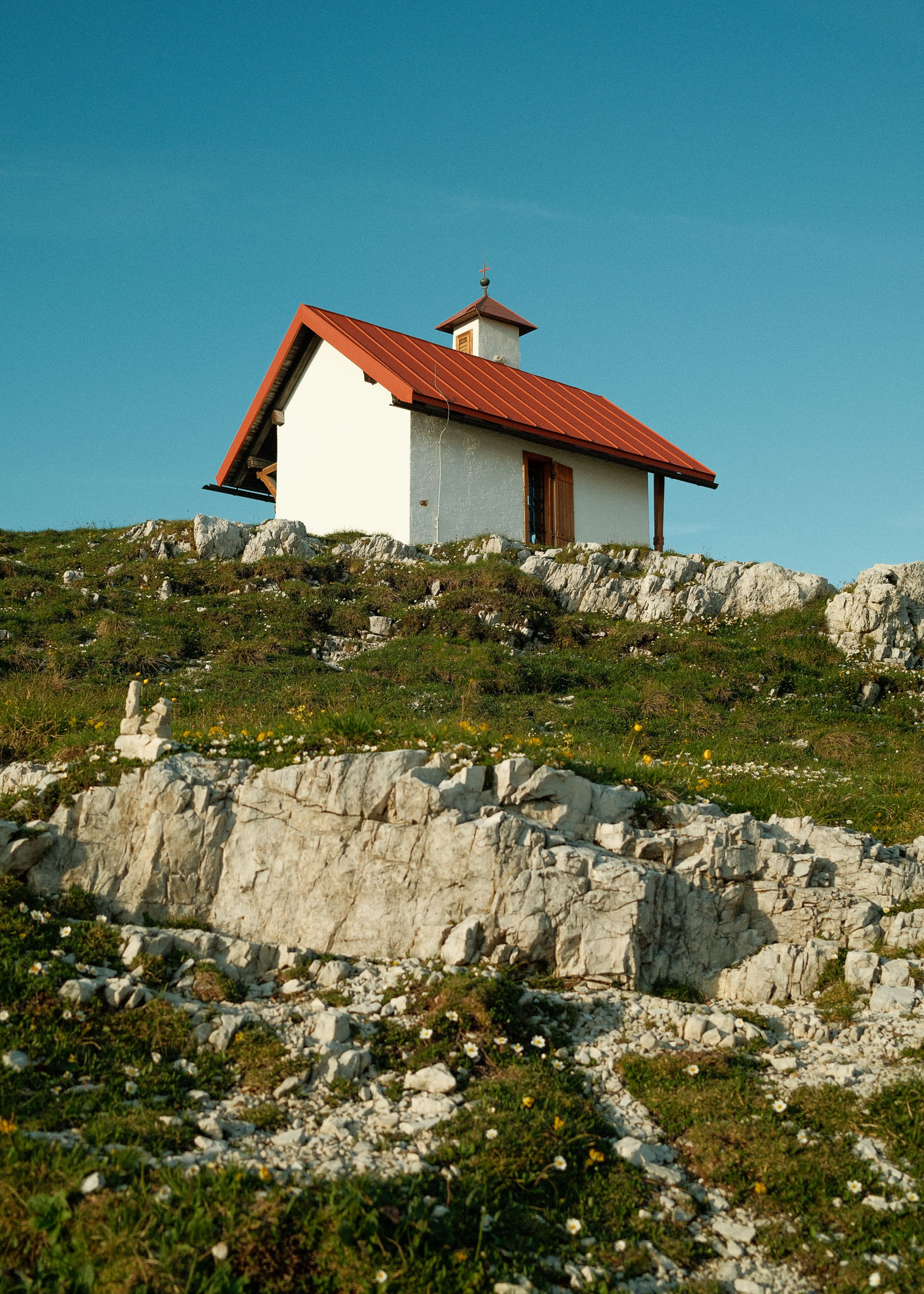 An alpine white and clay-coloured hut in the middle of the day. Taken on the Fujifilm X100VI by Hermann Furin.