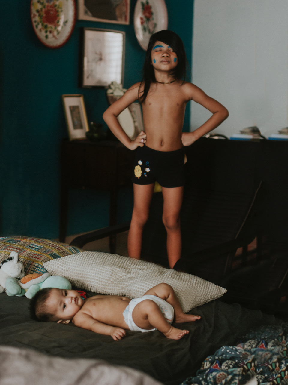 Ein Kind mit blauer Gesichtsbemalung steht über einem Baby, das in einem Bett liegt, aufgenommen von Lisha Zulkepli mit einer Canon EOS 700D