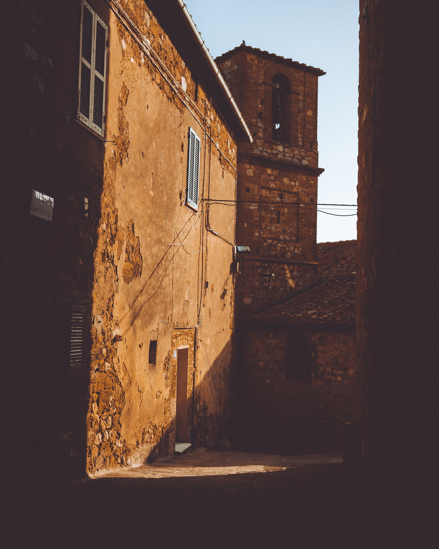 A street in Petrolo, Tuscany. A taller building appears in shadow whilst the wall on the street is in sunlight.