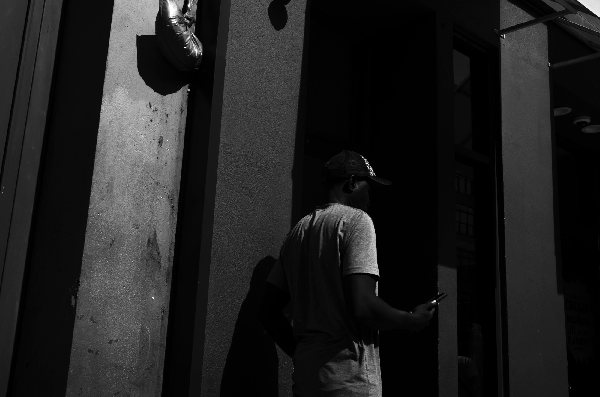 A black-and-white photo of a person in a hat standing by a wall