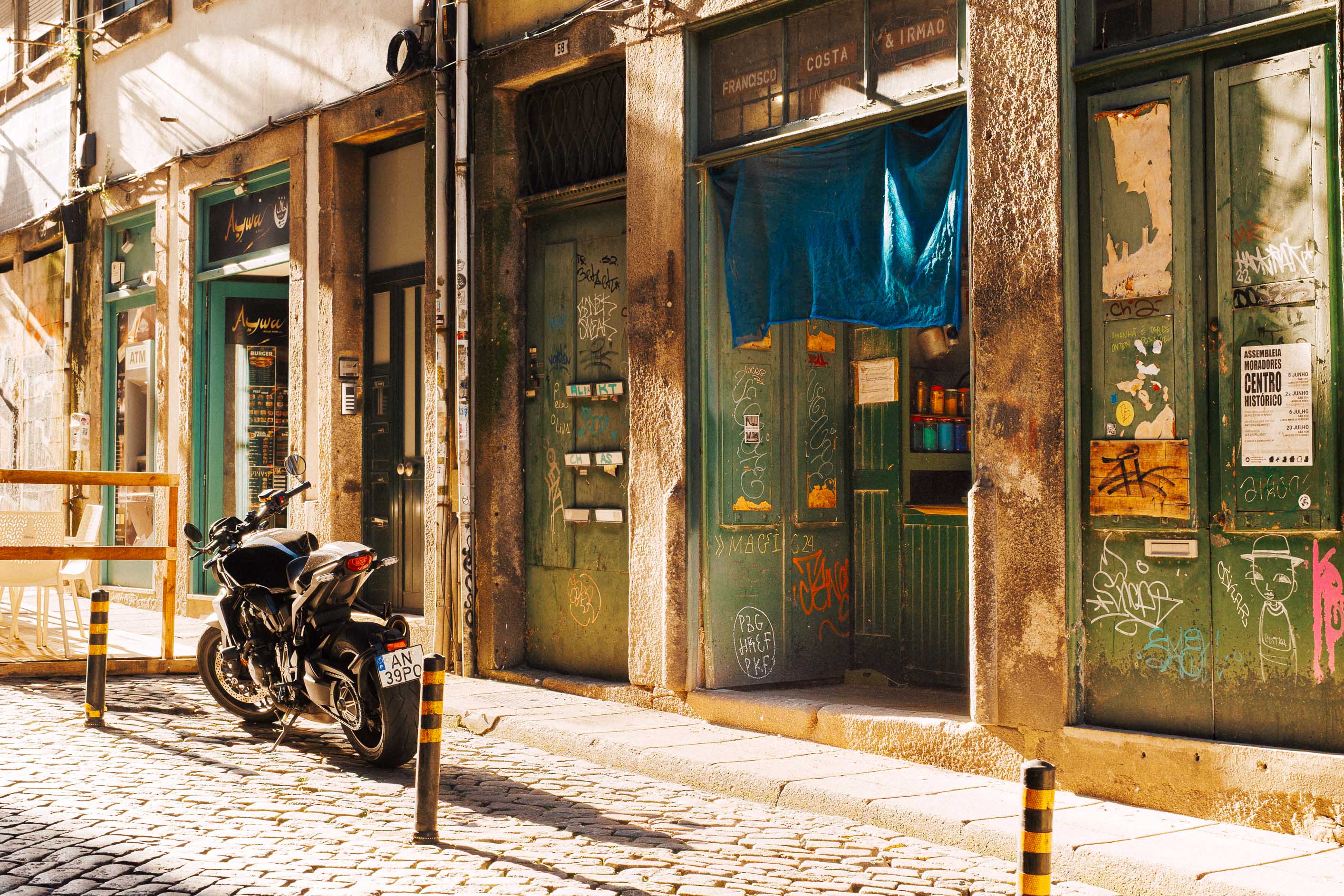 Eine Straße in Porto auf der die späte Abendsonne lange, warme Schatten wirft. Es sind ein Eingang zu einer alten Bar und ein geparktes Motorrad zu sehen. Aufgenommen von Connor Redmond mit der Sigma BF.