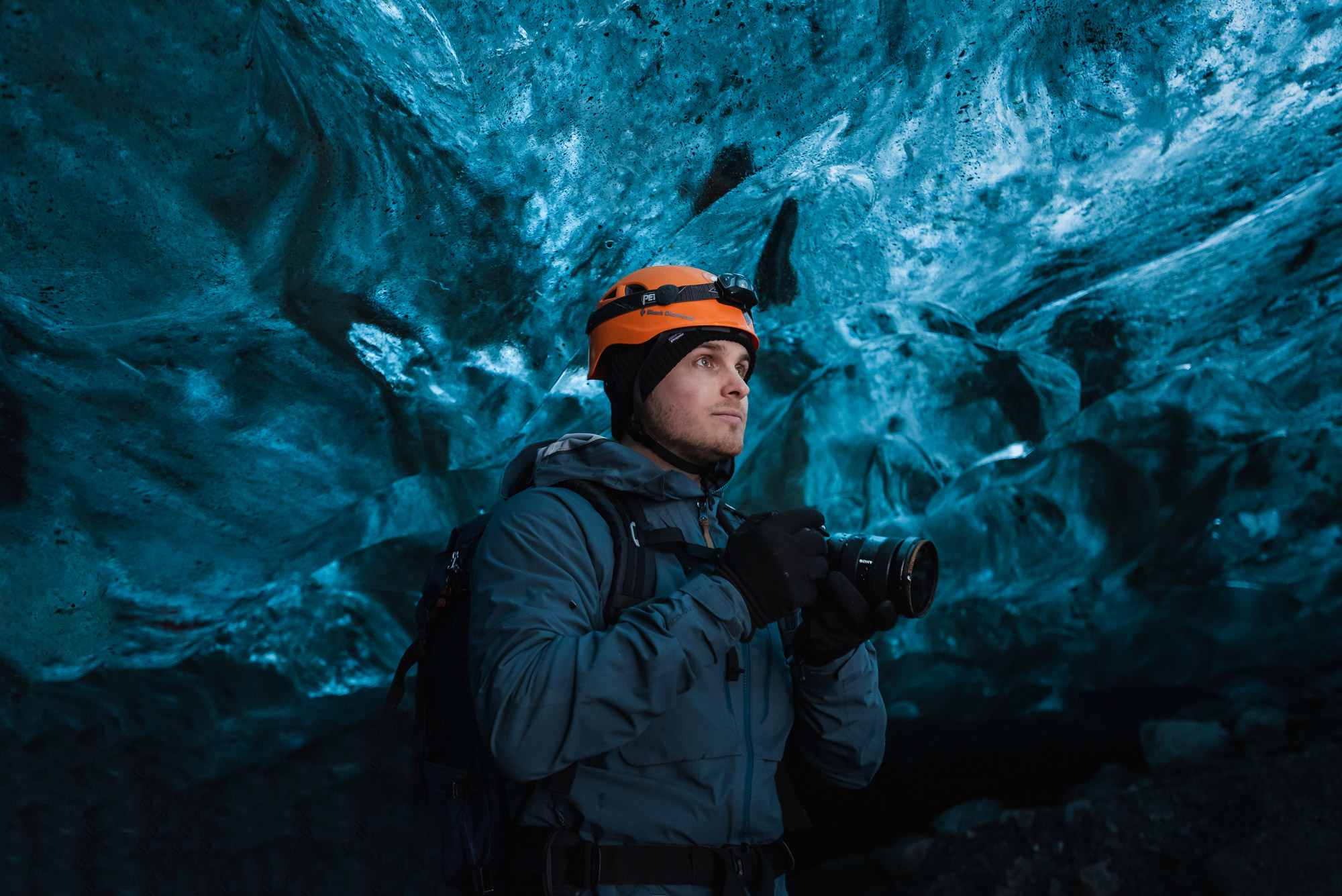 Marvin Kuhr with orange helmet and camera in hand in a glacier cave