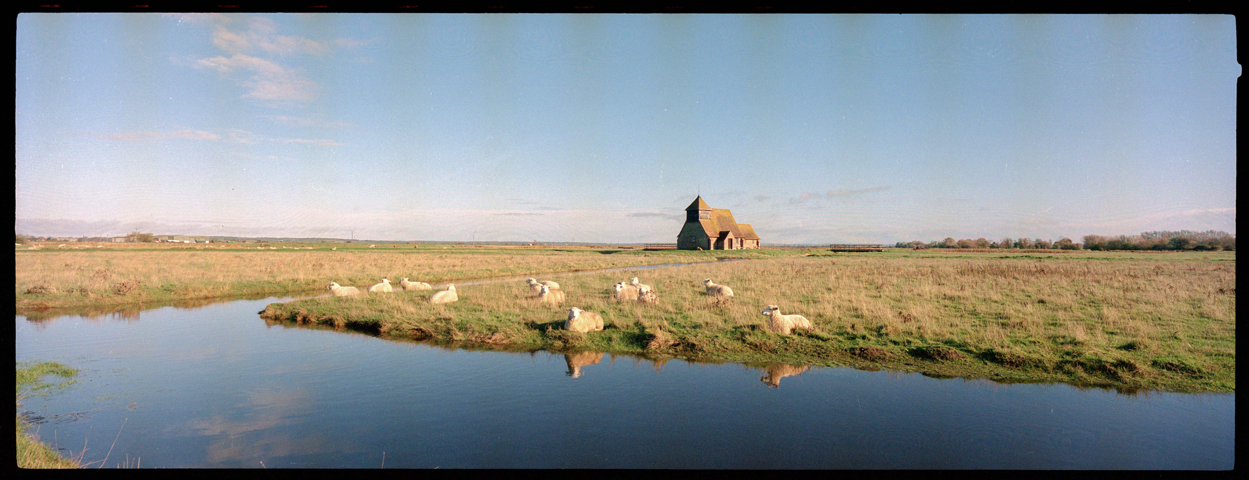 Ein Farbfilmfoto von einem Haus und Schafen an einem Fluss in Fairfield, Vereinigtes Königreich, aufgenommen mit einer Hasselblad XPan II von Ian Howorth