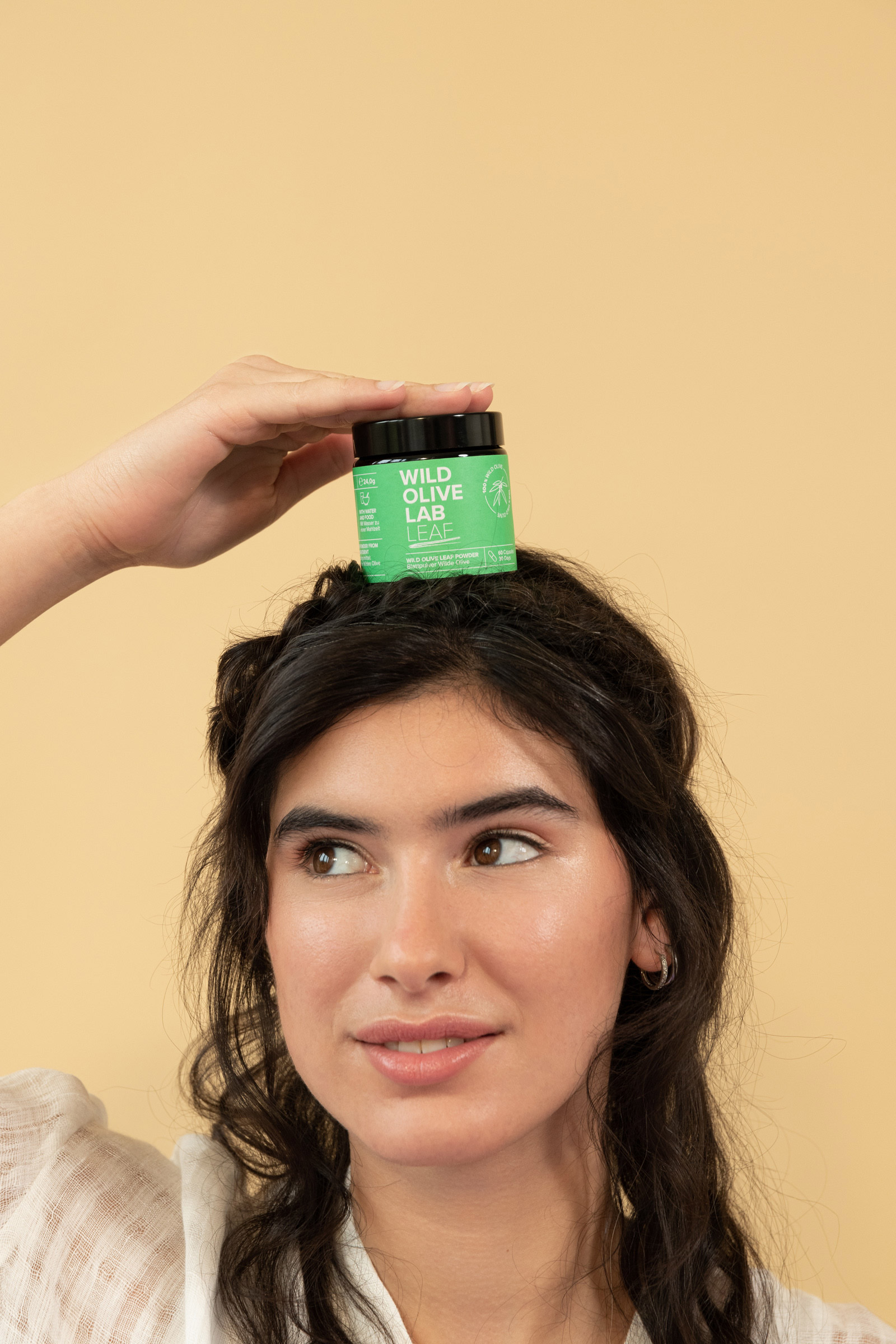Porträt von einer Frau, die eine kleine, grüne Dose der Marke "Wild Olive Lab" auf ihrem Kopf festhält, fotografiert von Anna Langer.


