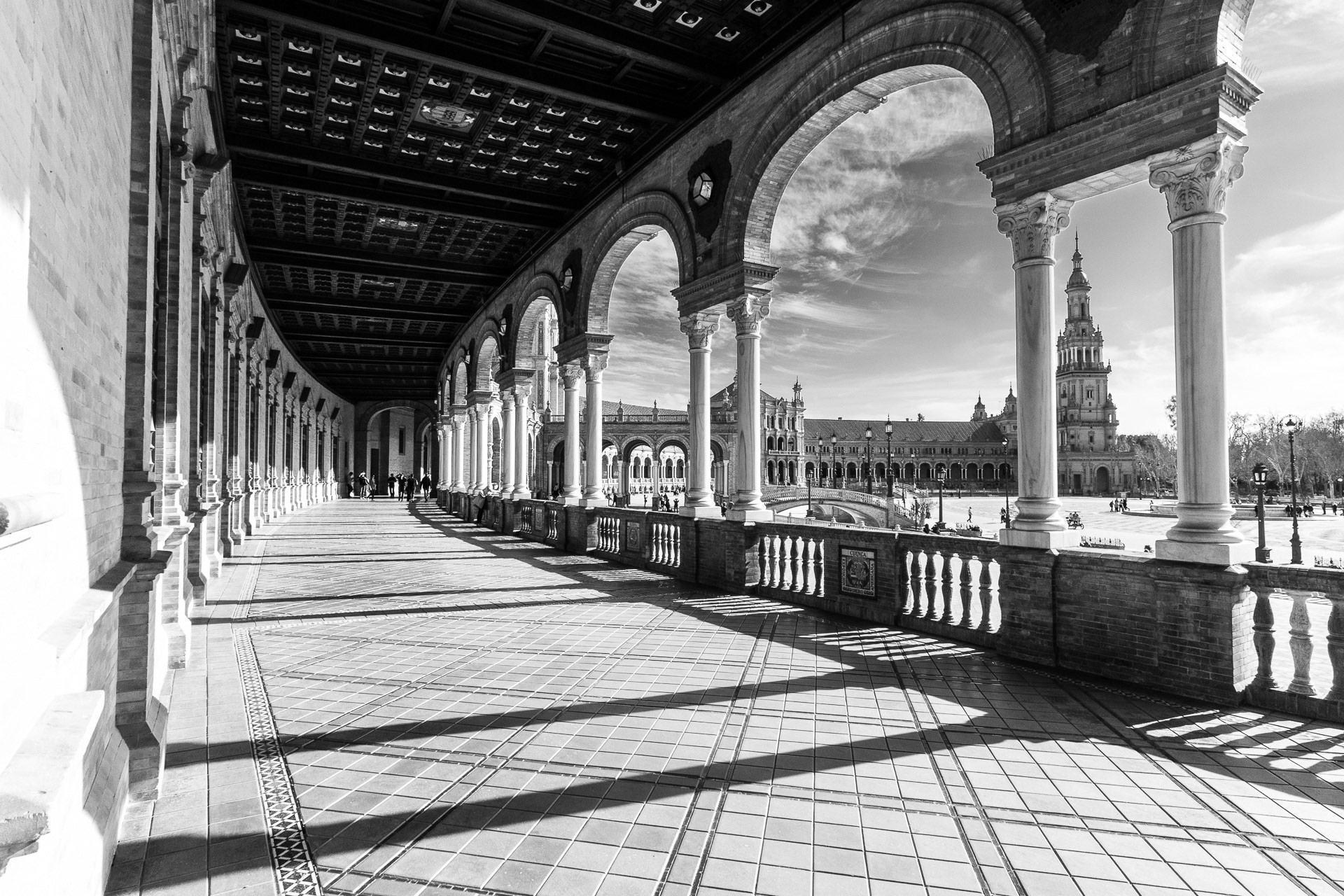 Zwart-witfoto van het Plaza de España in Sevilla, Spanje, waarop de noordelijke toren te zien is door de kolommen van de zuidvleugel van het Plaza, gefotografeerd door Maike Jarsetz.