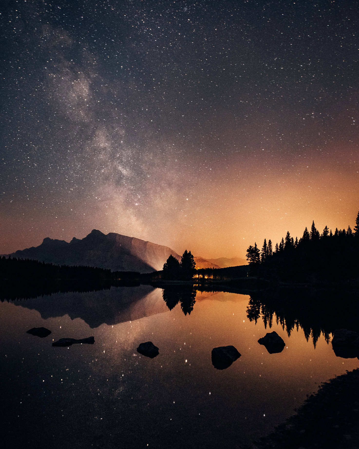 Two Jacks Lake in Banff National Park at night with reflection of starry sky and tree line, photo by Jude Allen.
