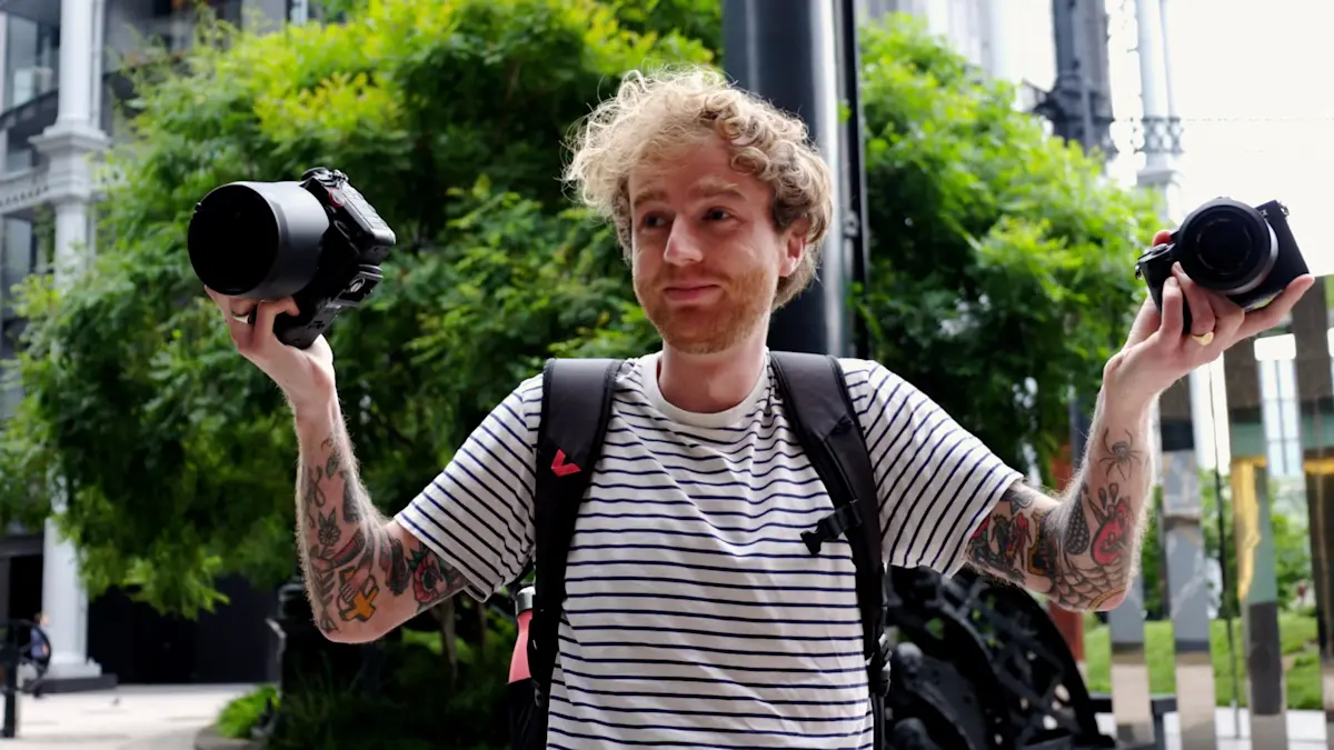 man holding up a mirrorless camera in one hand and a DSLR camera in the other hand