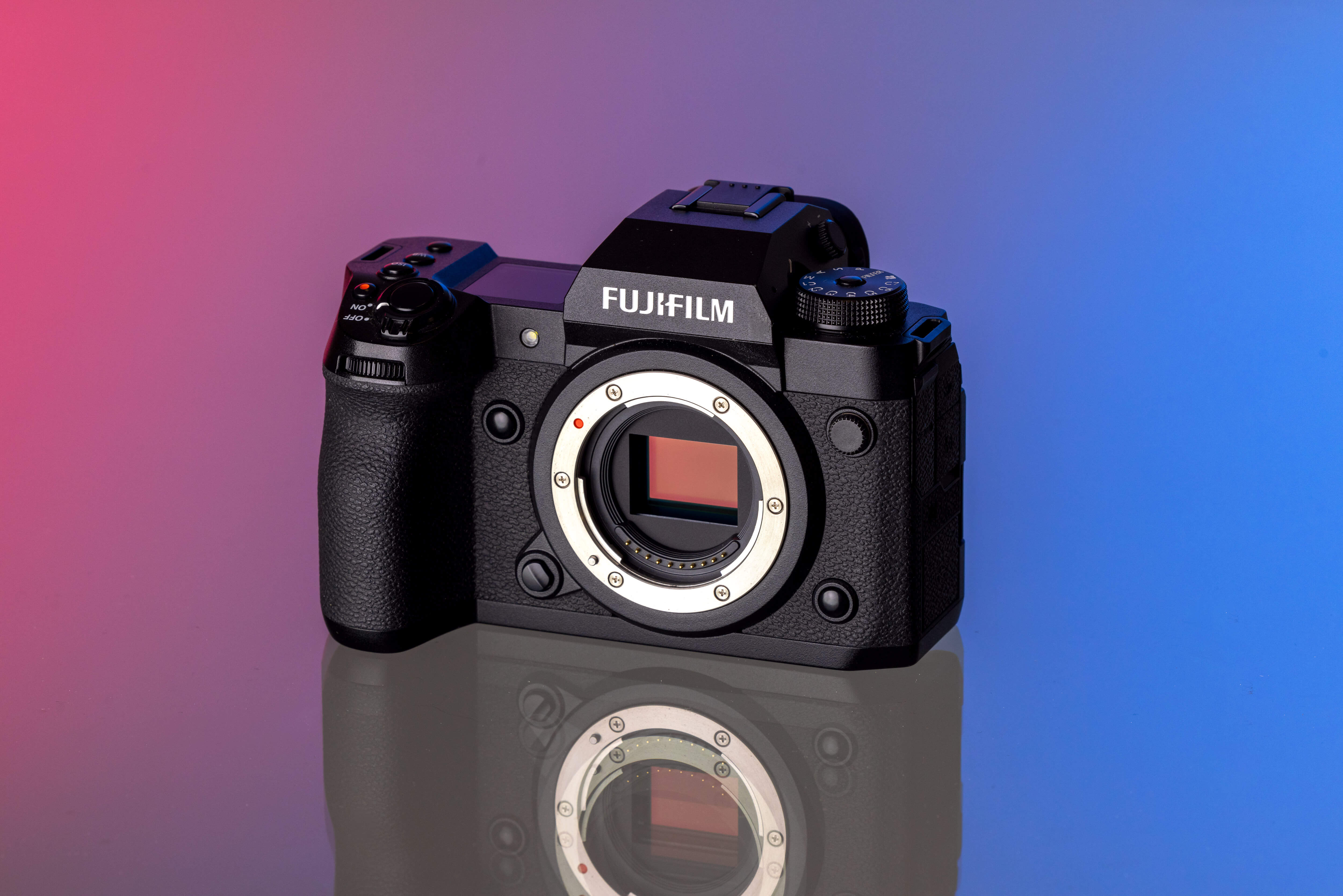 Un appareil photo Fujifilm X-H2 noir sur un fond éclairé en studio avec des tons rose et bleu.