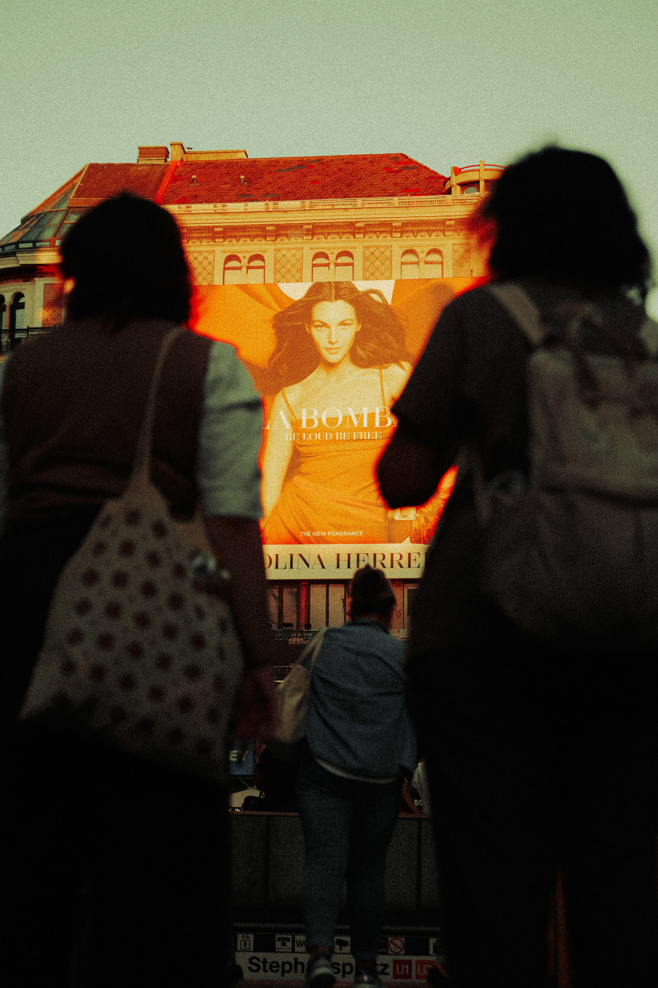 Kreative Streetfotografie in Wien mit Passant:innen, die den U-Bahnhof Stephansplatz betreten. Im Hintergrund, eine von der warmen Abendsonne beleuchtete Werbetafel. Aufgenommen von Dhan Limwattana mit einer Nikon Z5 II.
