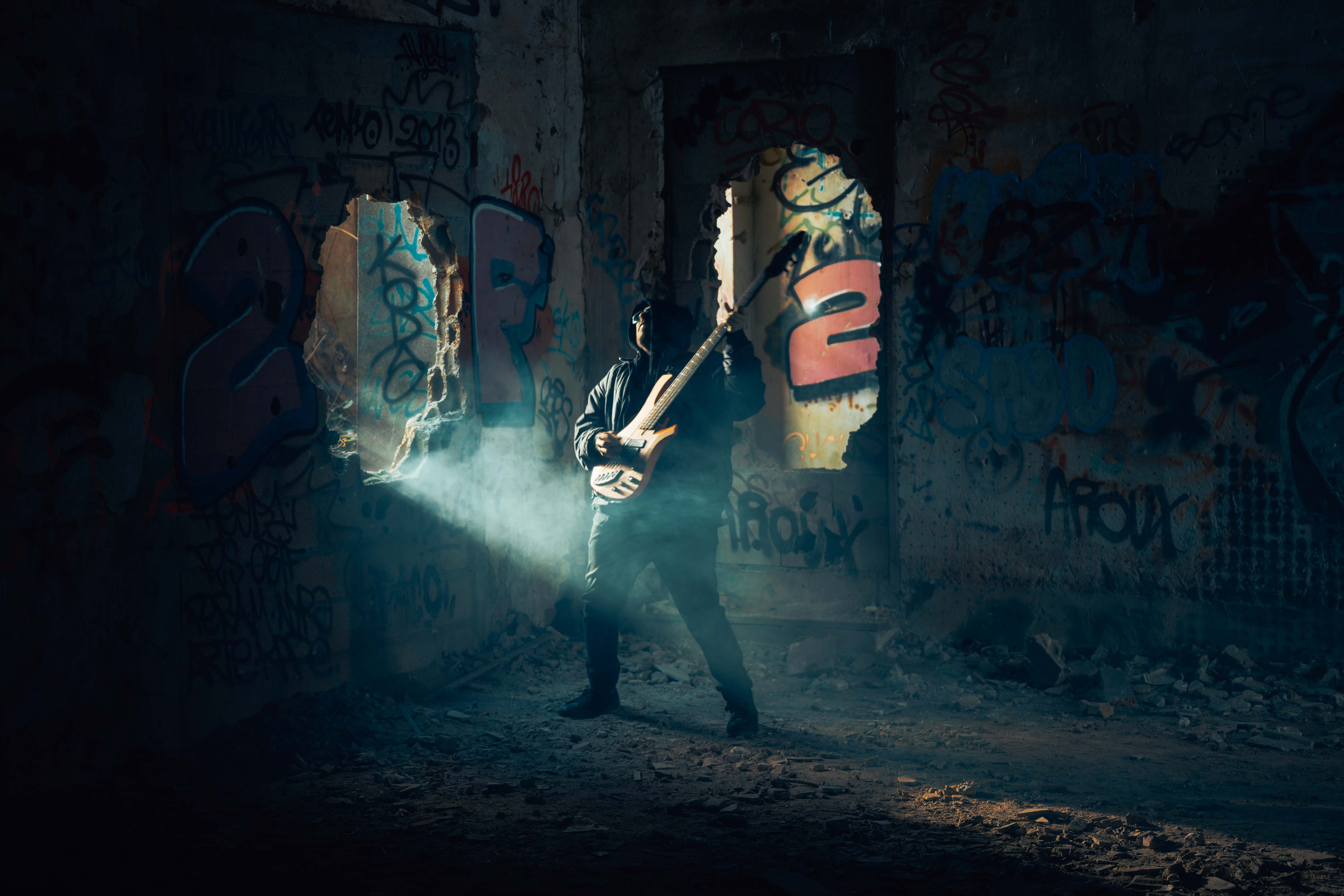 A bassist performs in a dark, graffiti-covered building as a beam of light cuts through smoke behind him, creating a dramatic music video scene. Photo taken by Lukas Davos. 