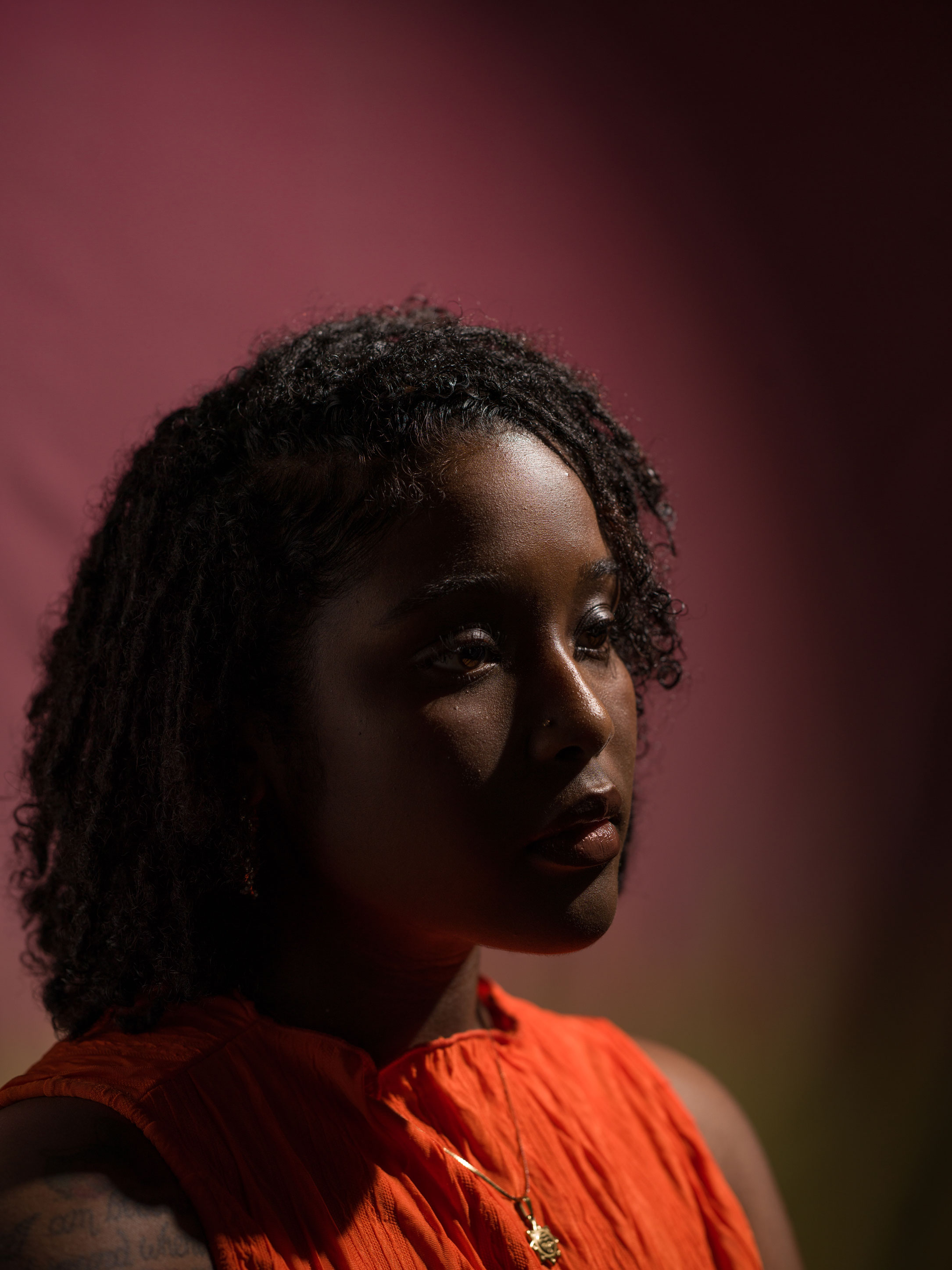 Portrait of a person with curly black hair and orange shirt using short lighting technique. Taken by Kaylah Sambo on a Hasselblad X1D-50c.