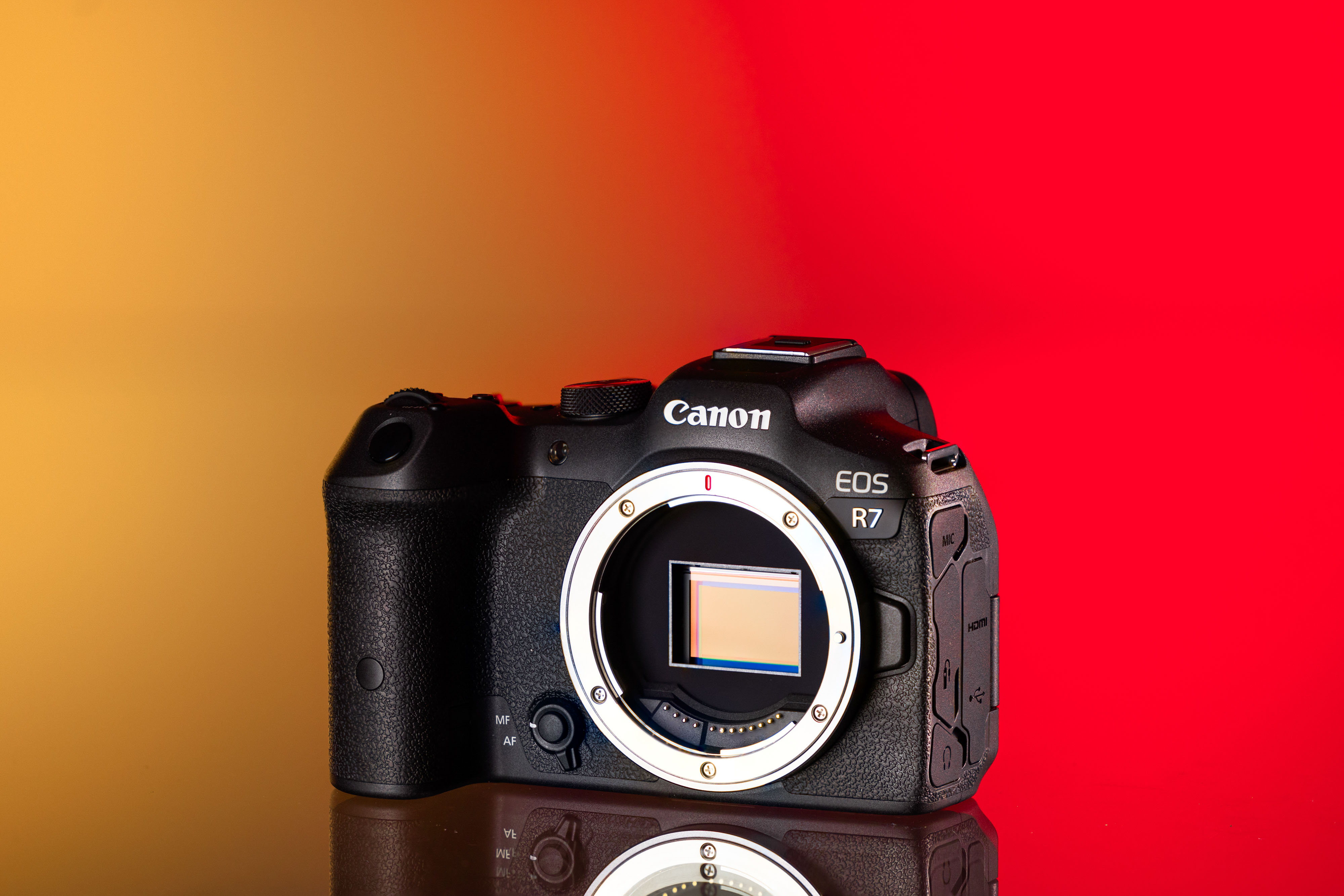 Cámara Canon EOS R7 de segunda mano sobre un fondo amarillo y rojo
