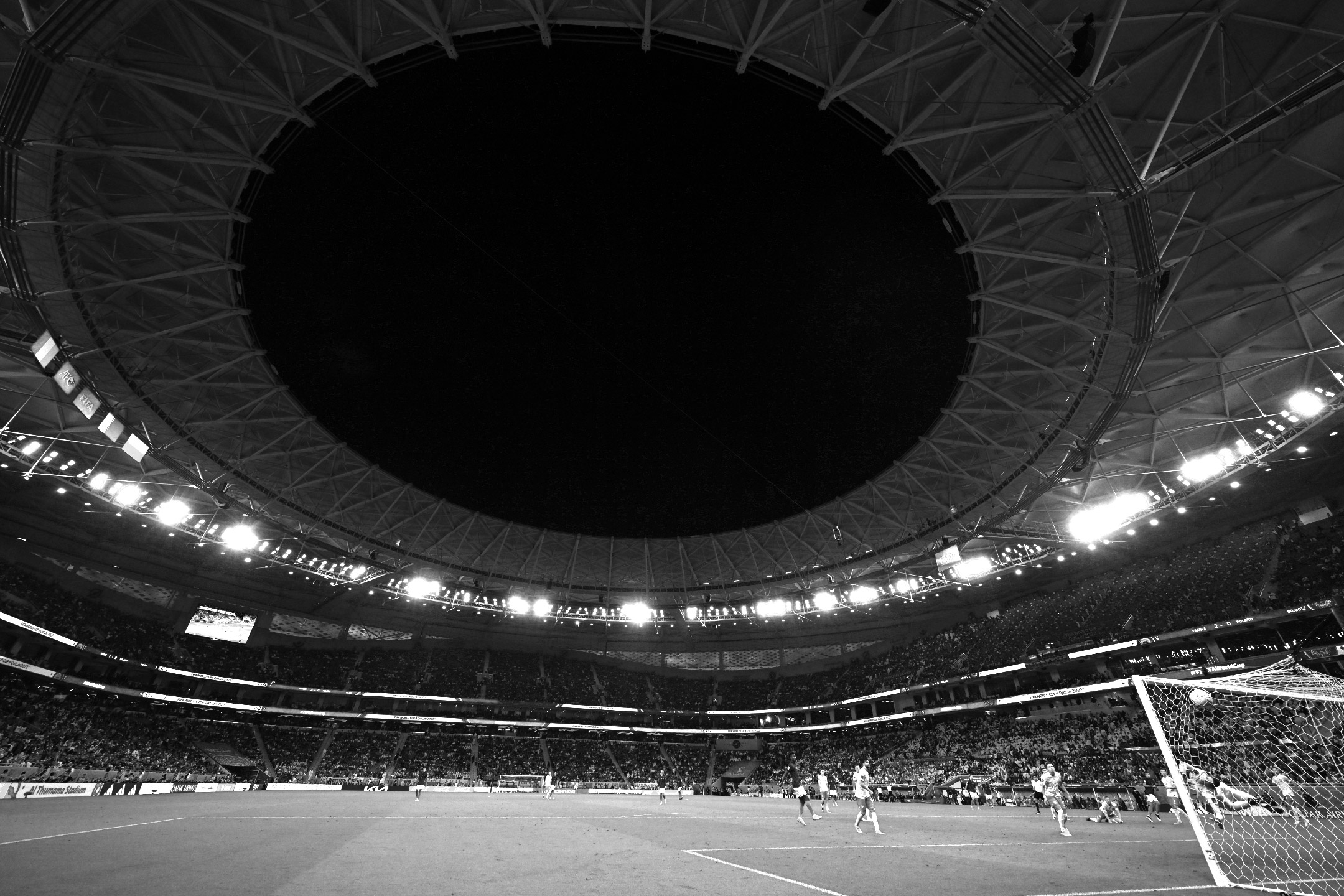 Ein Schwarz-Weiß-Foto des runden Daches des Al-Thumama-Stadions, das sich über Kylian Mbappé von Frankreich erhebt, als er im Achtelfinale der Fußball-Weltmeisterschaft 2022 gegen Polen ein Tor erzielt, aufgenommen von Ryu Voelkel mit einer Nikon Z9.